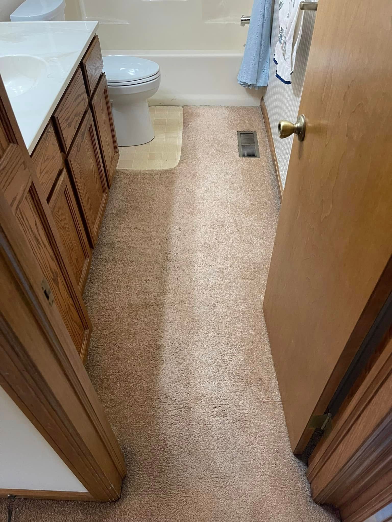 Bathroom with speckled tan and brown flooring, brown cabinets, and a toilet.