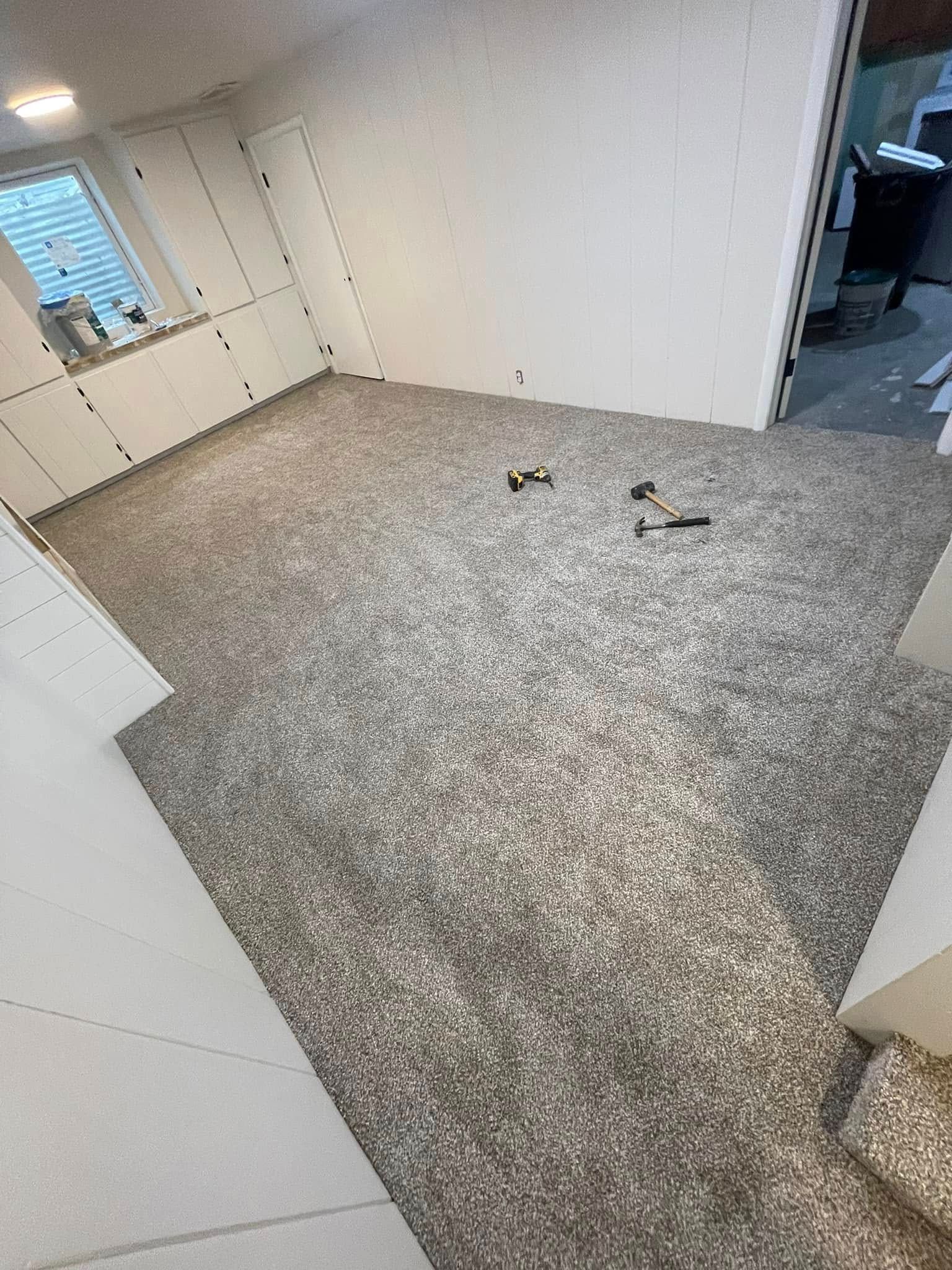 Room with light gray speckled carpet and white walls. Tools are on the floor.