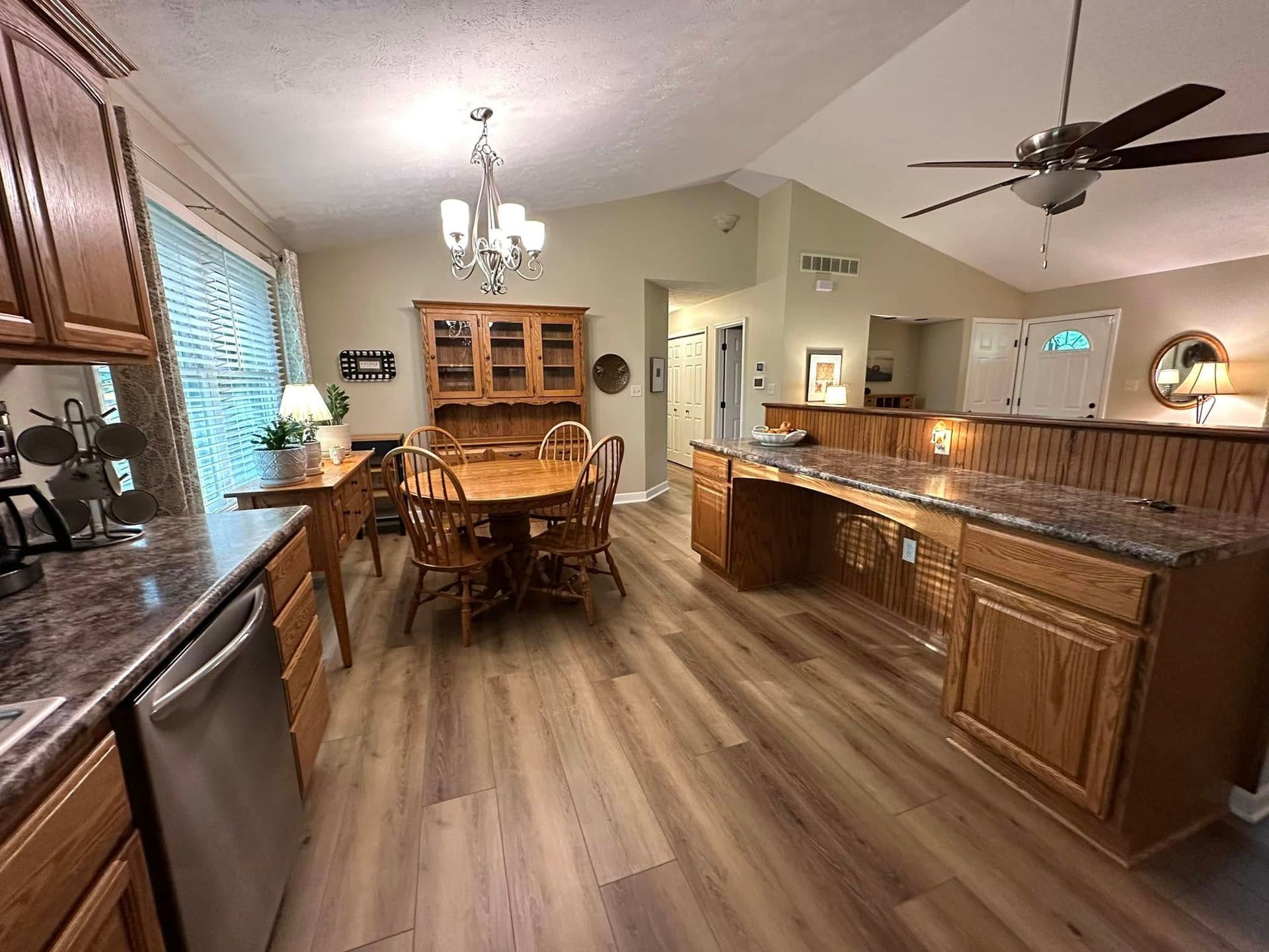 Kitchen and dining area with wood cabinets, table, and island; a chandelier and ceiling fan are visible.