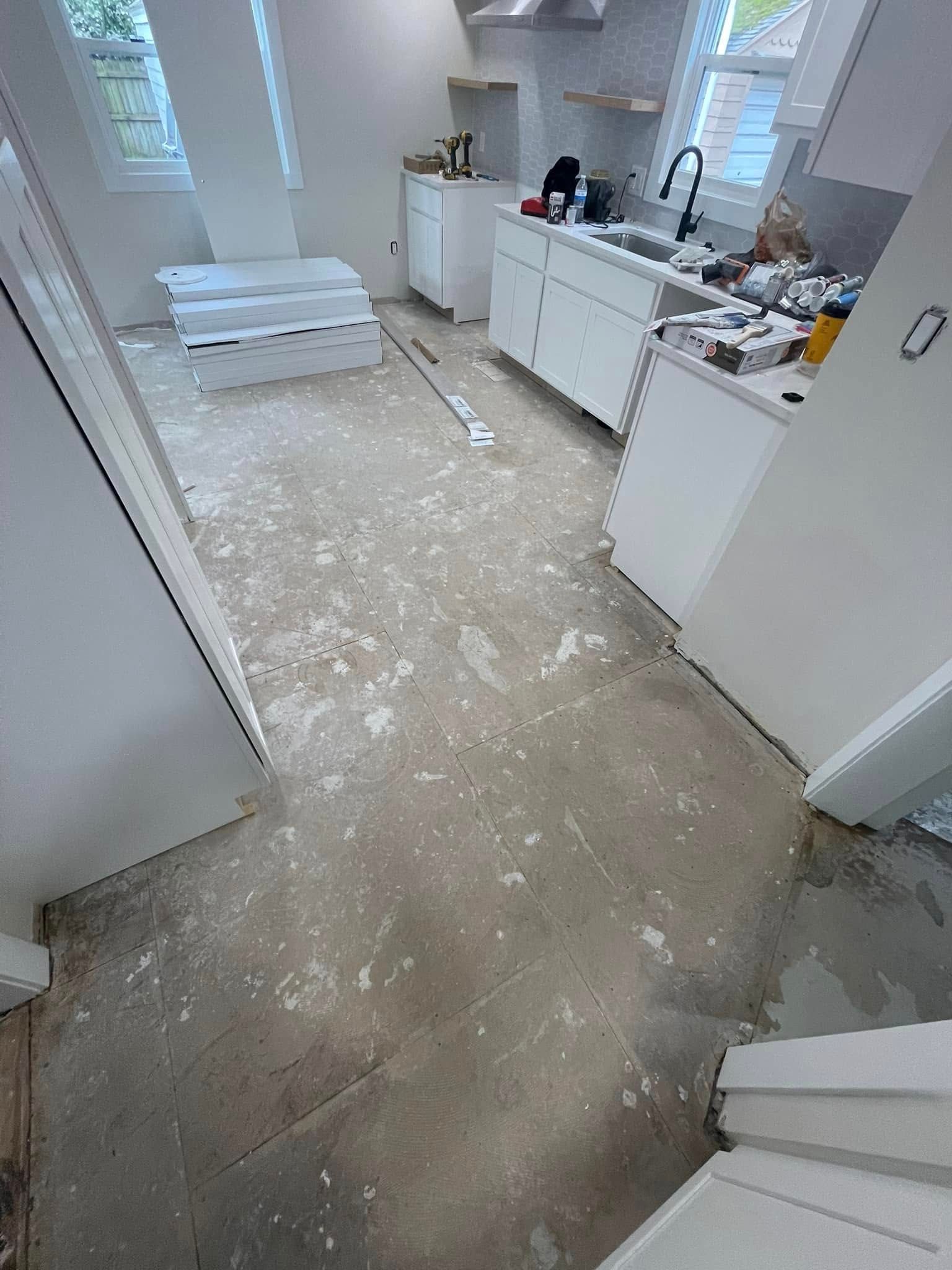 Kitchen renovation in progress, white cabinets, debris on the floor, construction materials.