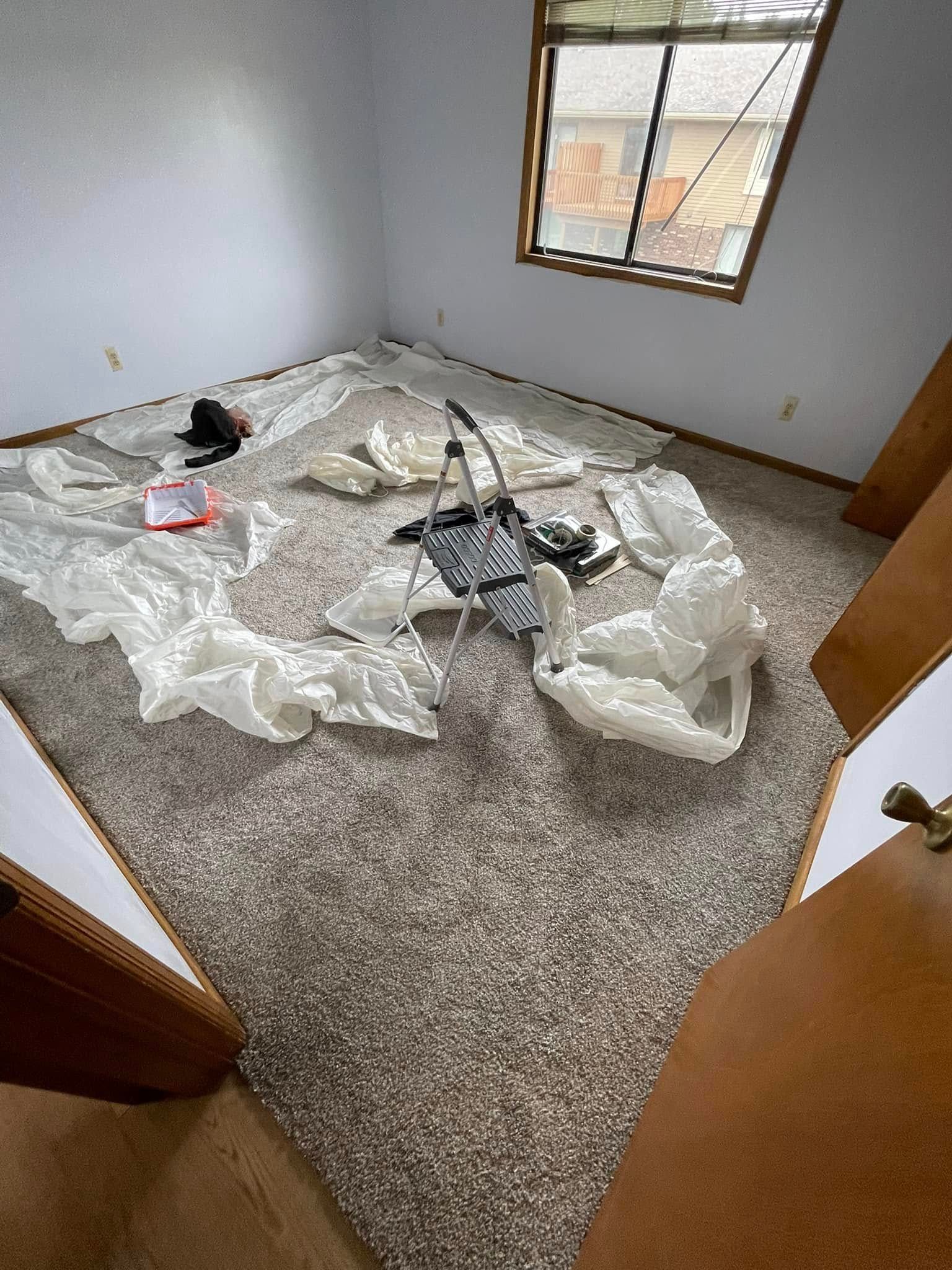 Room with light carpet, a window, and scattered items, including white bags and a handbag.