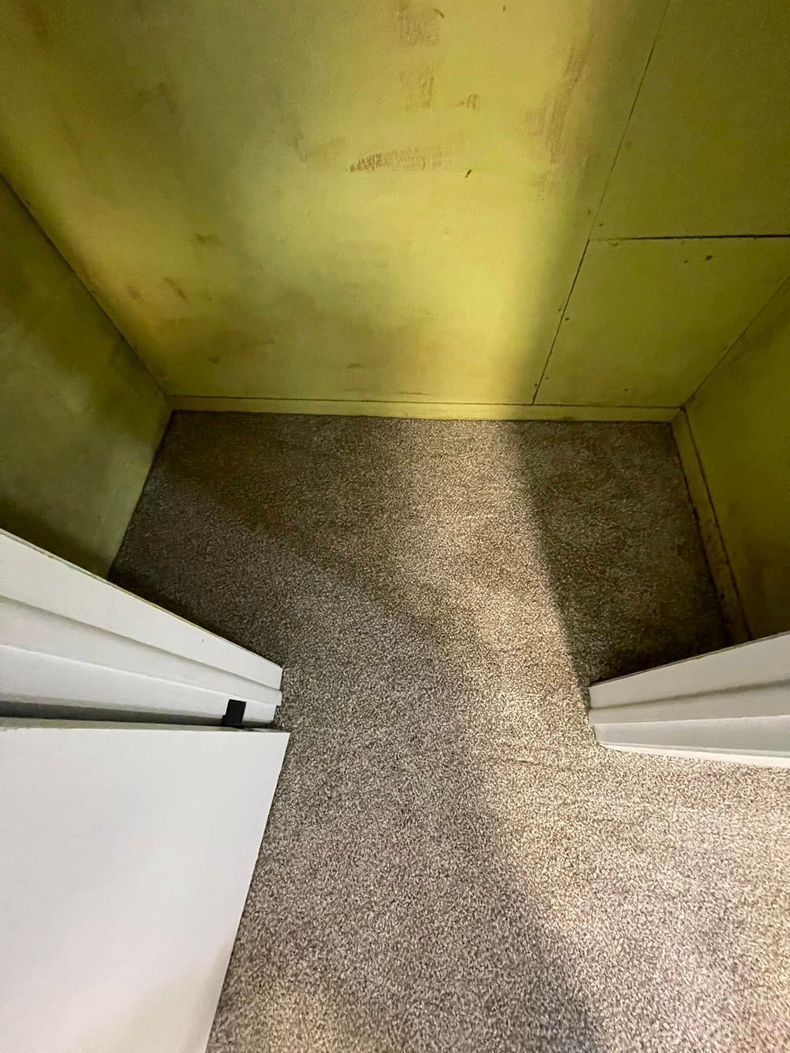 Inside of a cabinet with light shining on a speckled floor. The walls are yellow. Two doors on left and right.