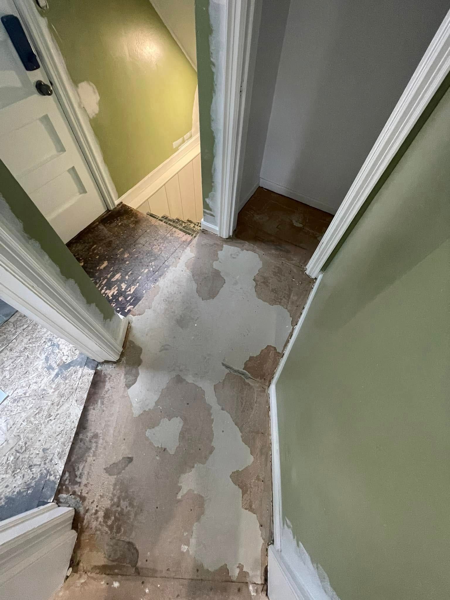 Hallway with peeling floor and green walls. White trim and doorways.
