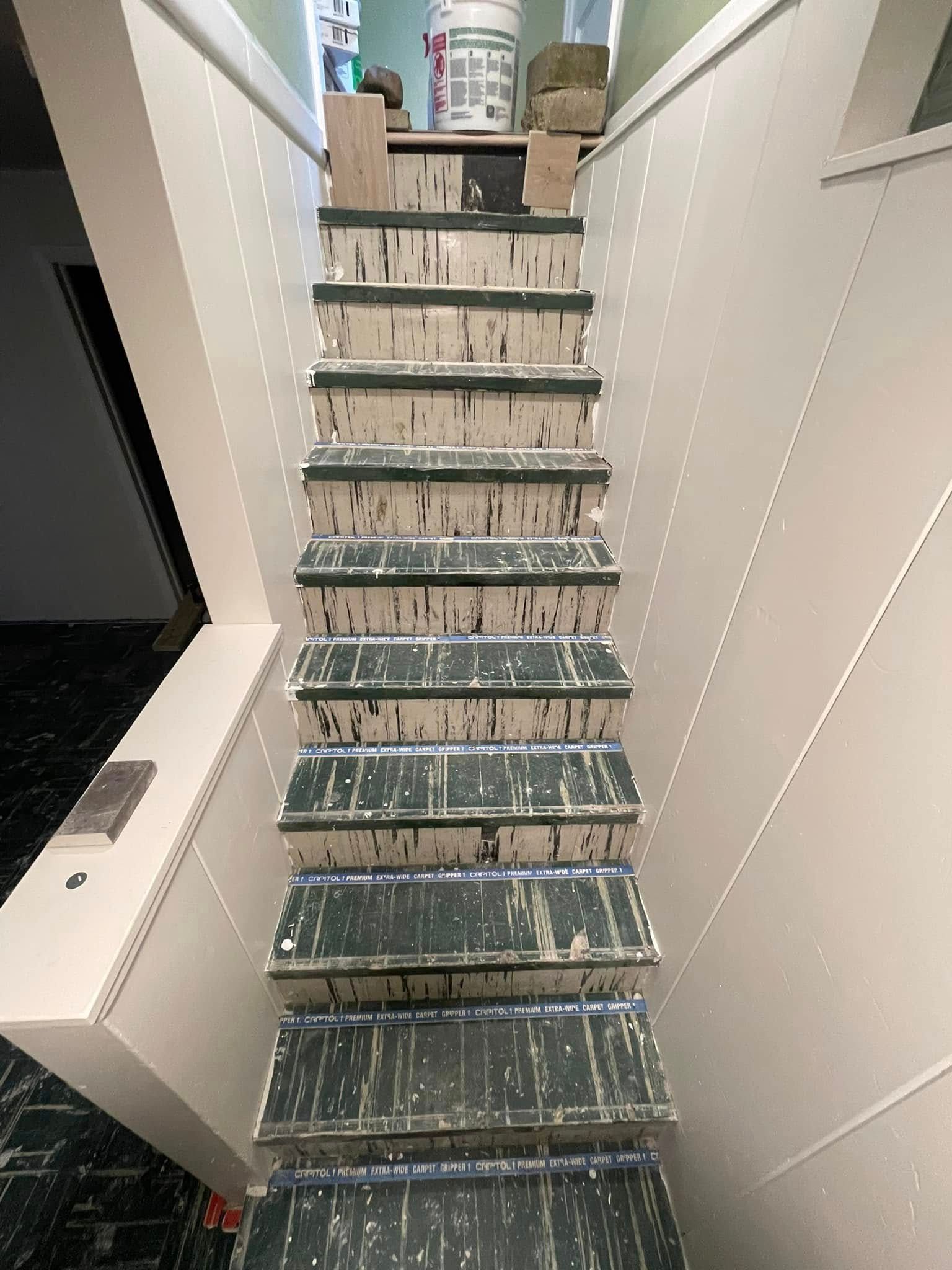 View of a worn staircase, white walls, green-painted steps, and a bucket at the top.