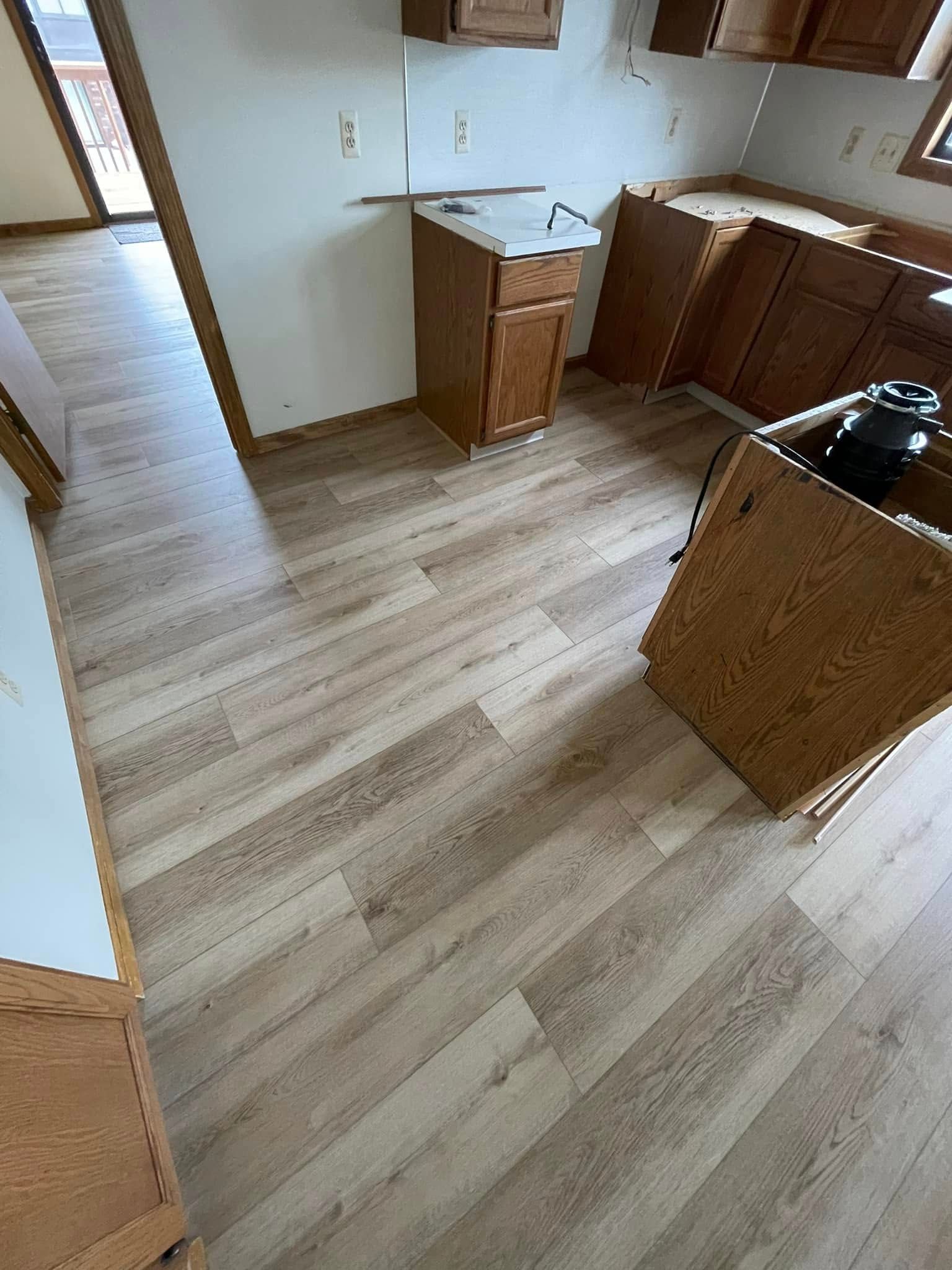 Kitchen with light wood-look flooring and dark cabinets; unfinished walls and some appliances are visible.
