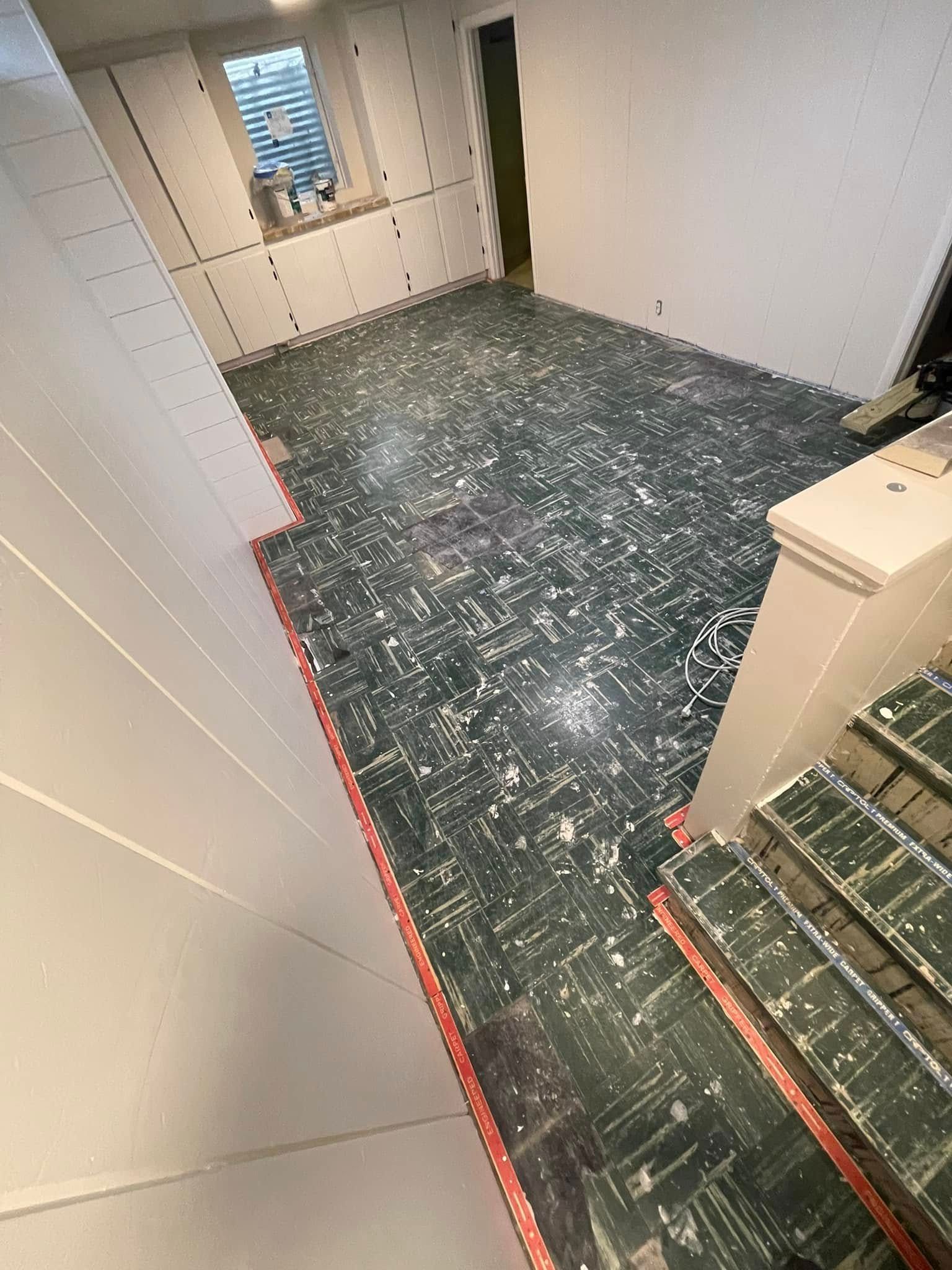 Basement renovation in progress with green and white flooring and red edging. White walls and stairs visible.