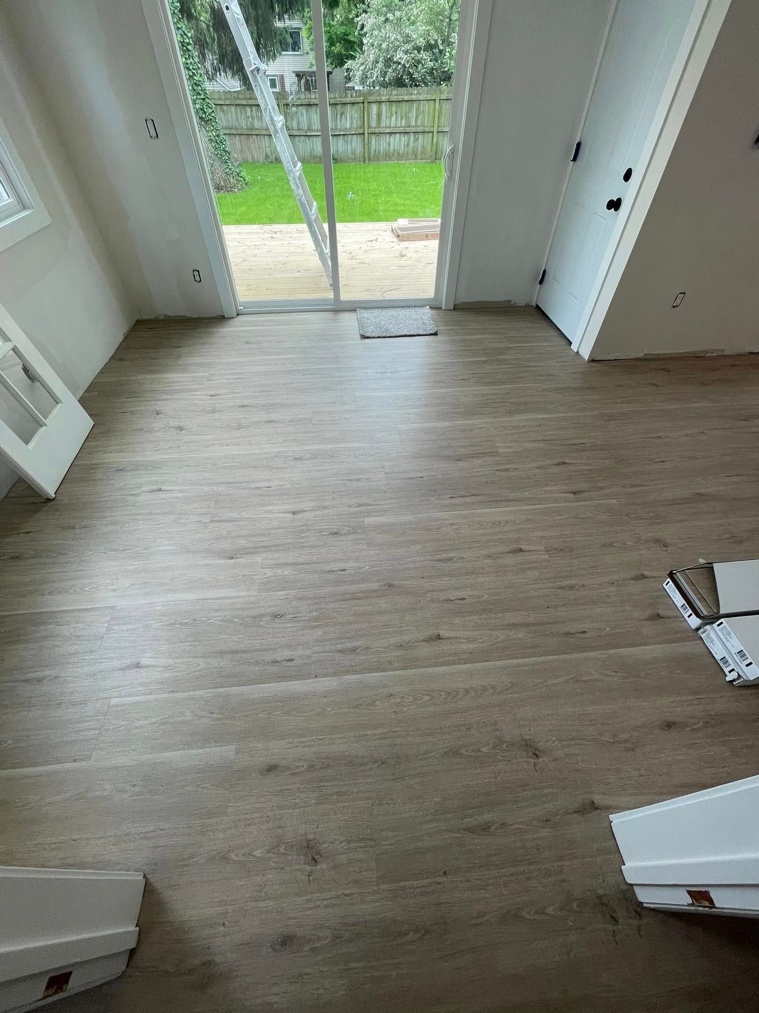 Room with light wood-look flooring, open glass door to backyard, white walls, and trim pieces on the floor.
