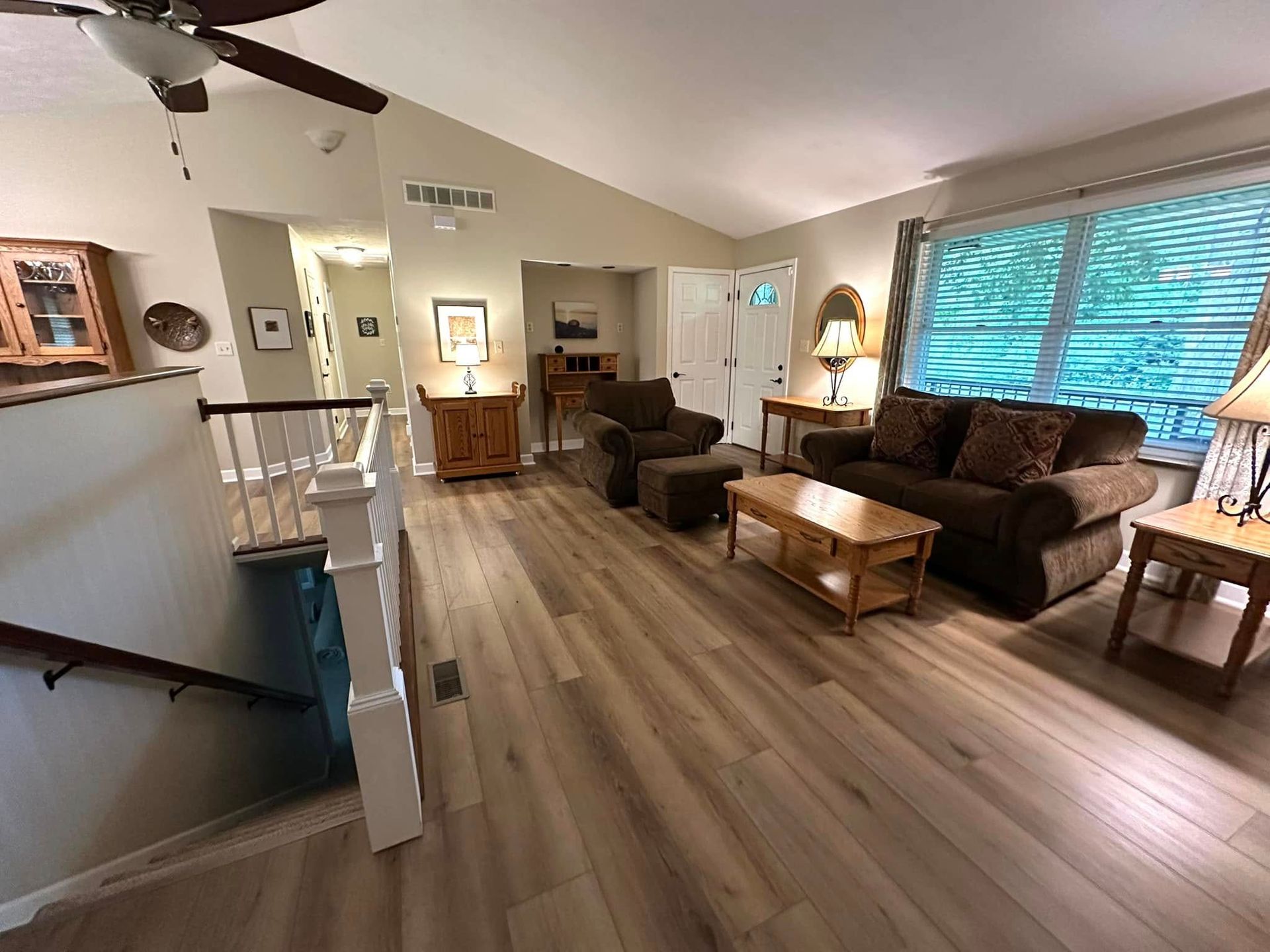 Living room with brown furniture, hardwood floors, and a stairway.