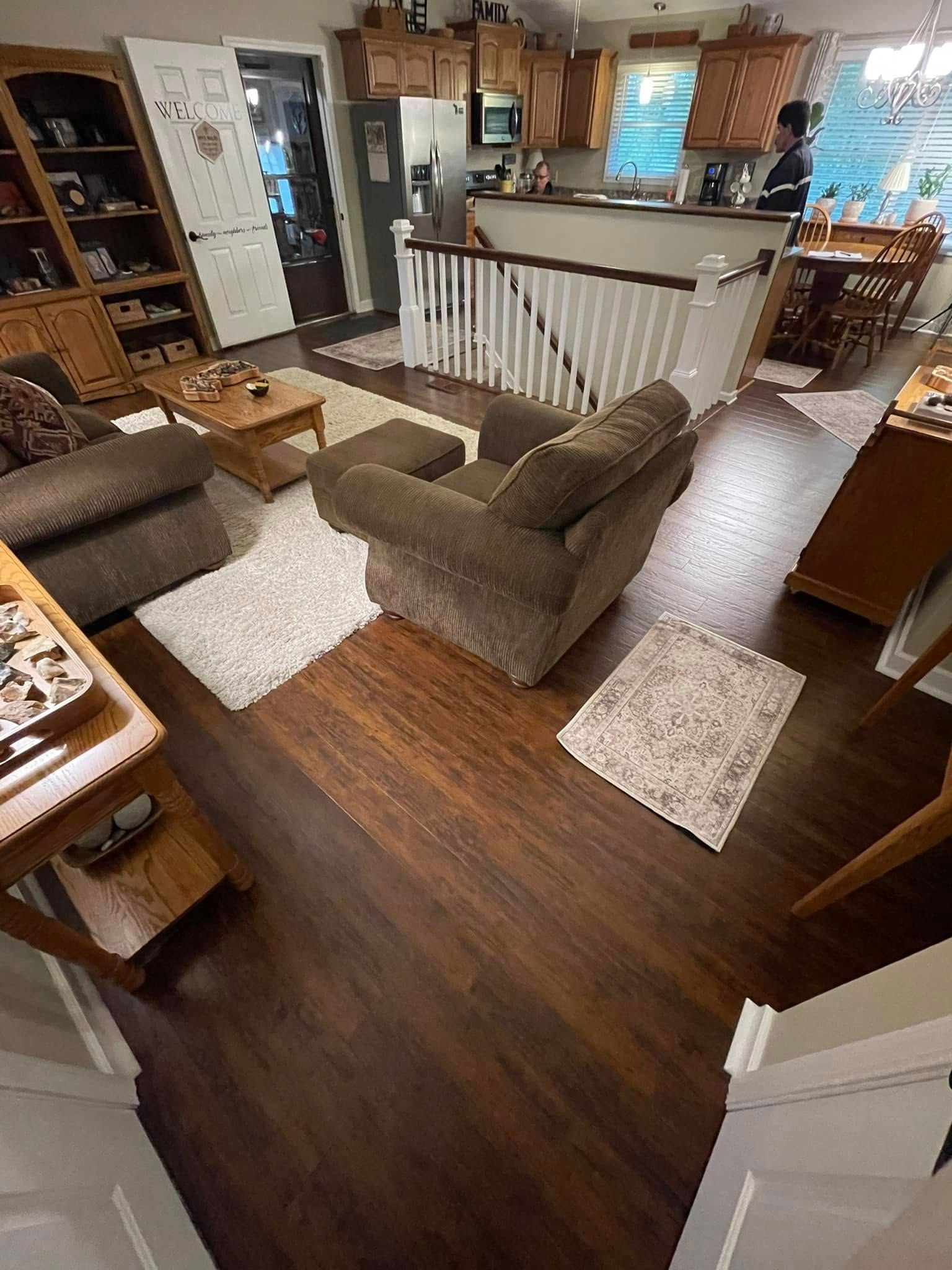 Living room with brown recliner, rugs, wood floors, and a staircase.