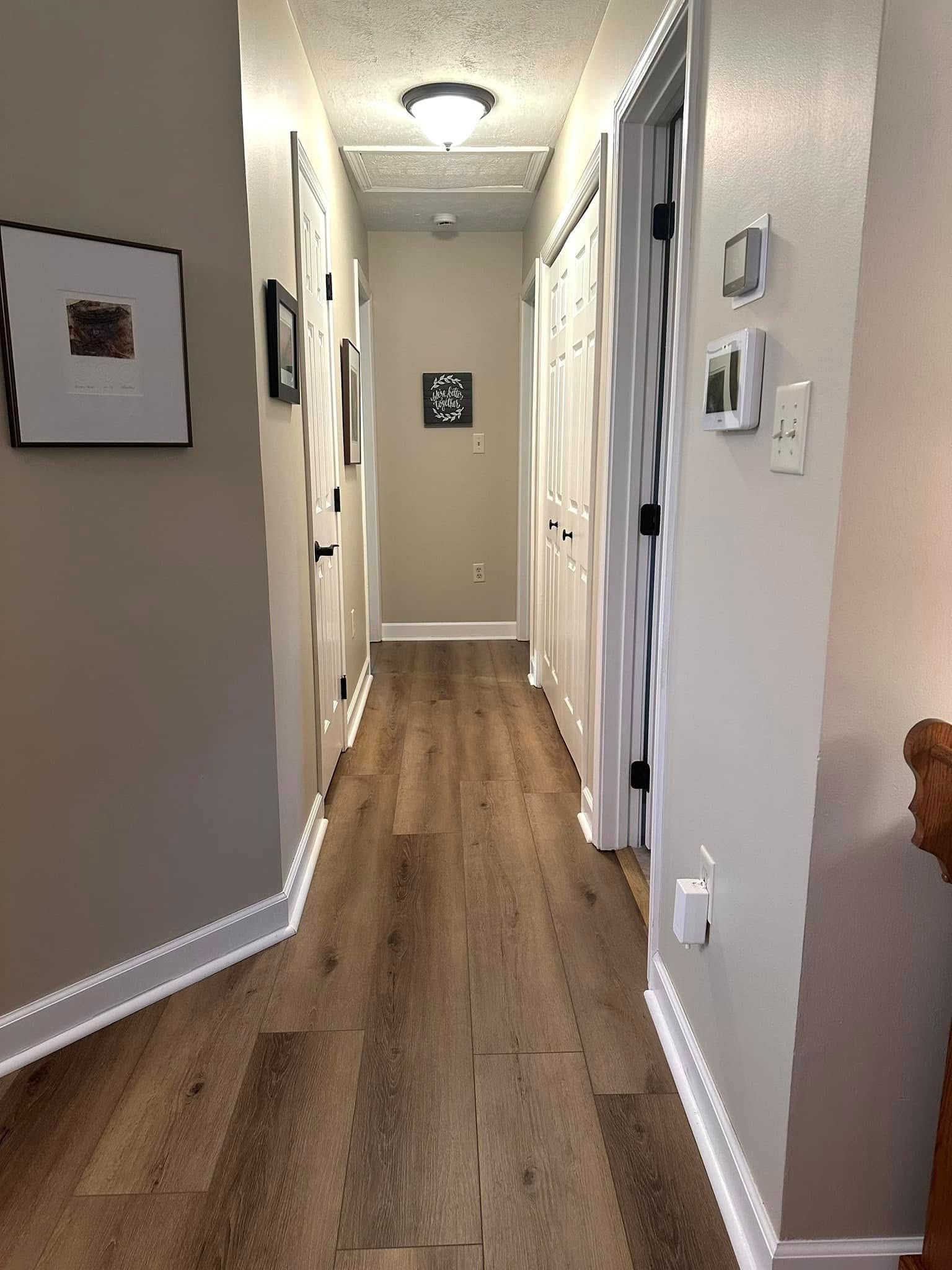 Narrow hallway with brown wood-look flooring, beige walls, and white trim. Several closed doors line the walls.