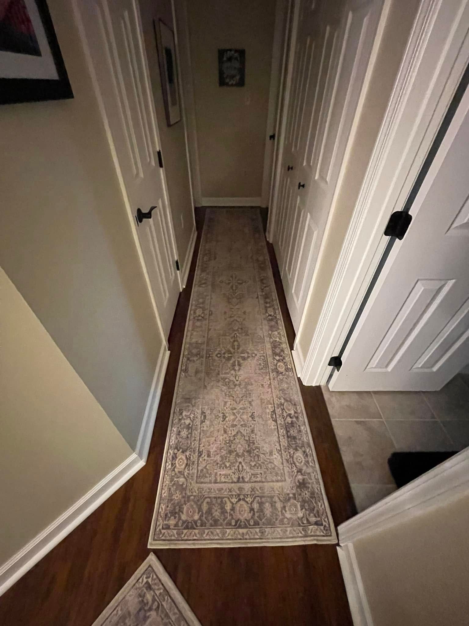 Narrow hallway with a long rug, white doors, and dark hardware.