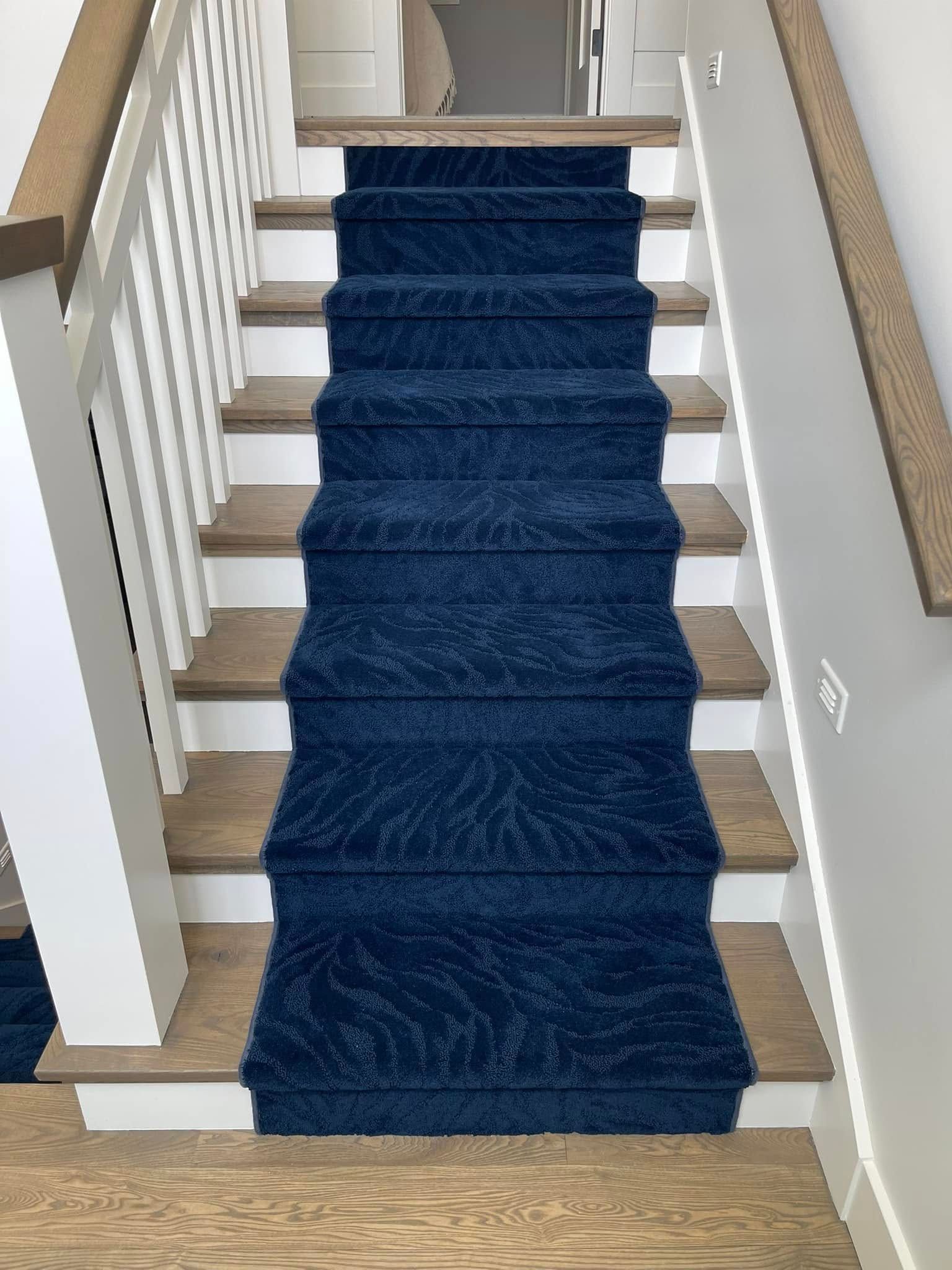 Navy blue carpet runner on wooden staircase with white railing.