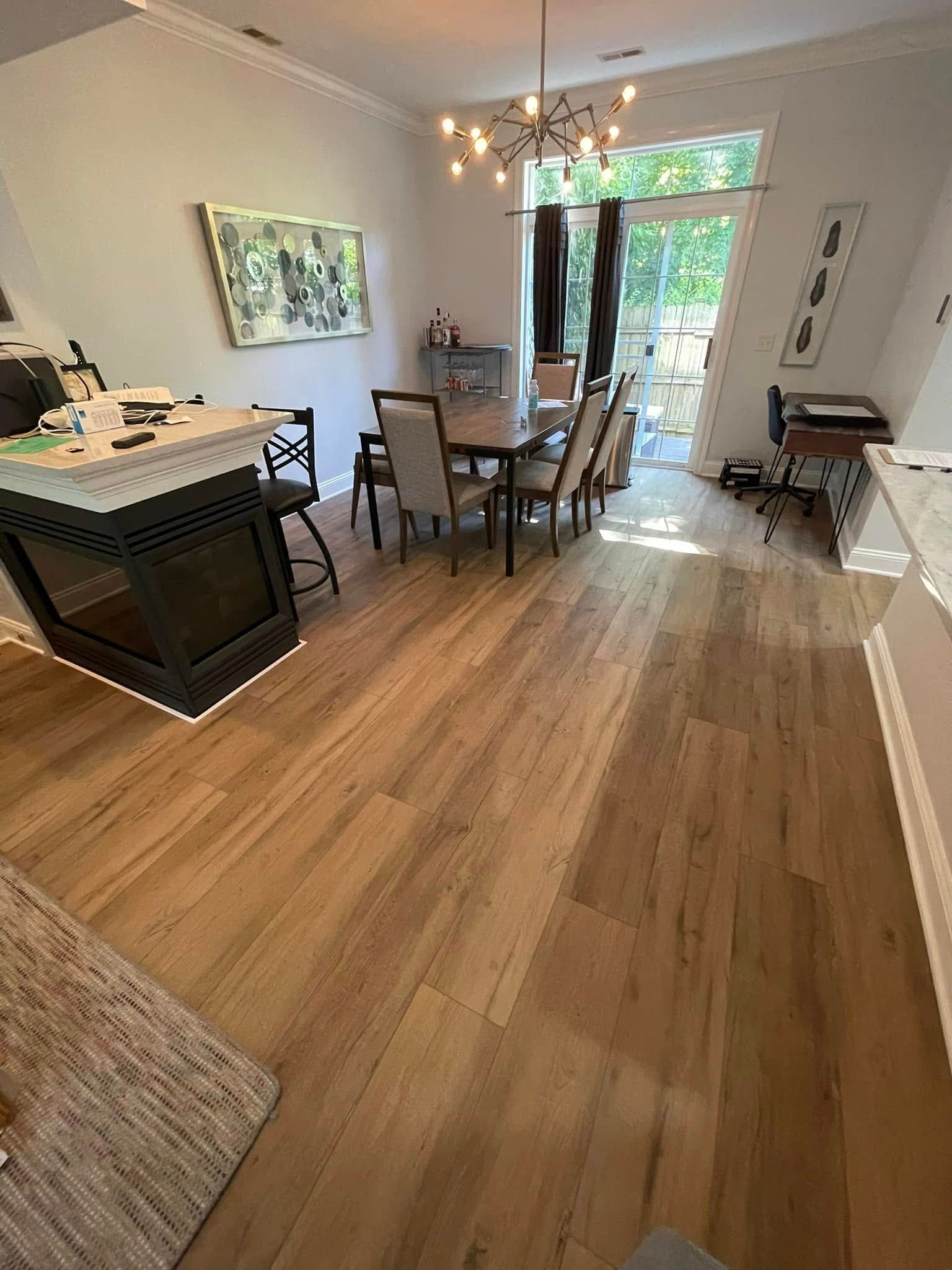 Wooden floor dining room with table, chairs, fireplace, and chandelier. Large window and artwork on the wall.