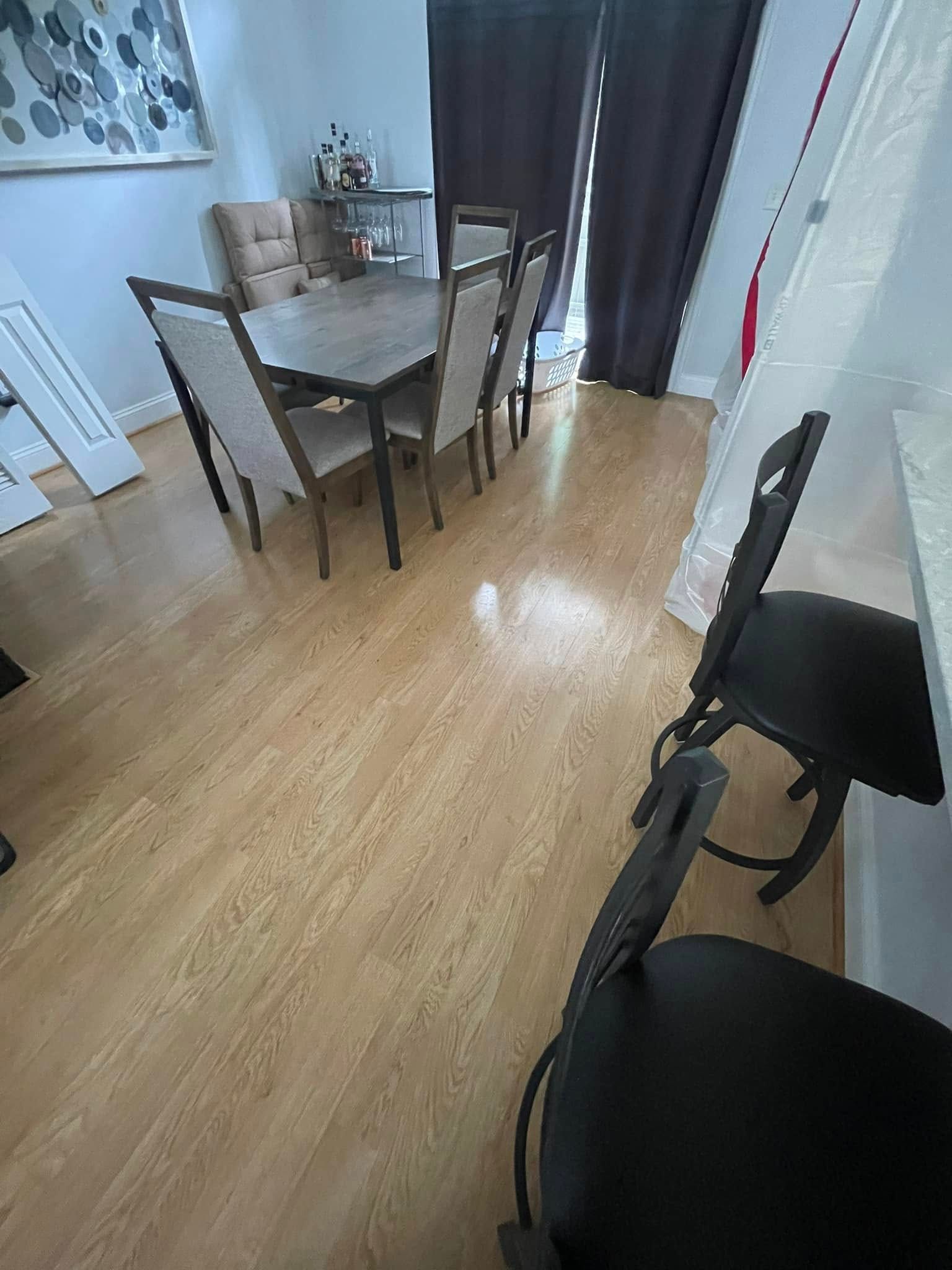 Dining room with wooden floor, table and chairs.  Dark curtains in background, counter with black chairs in foreground.