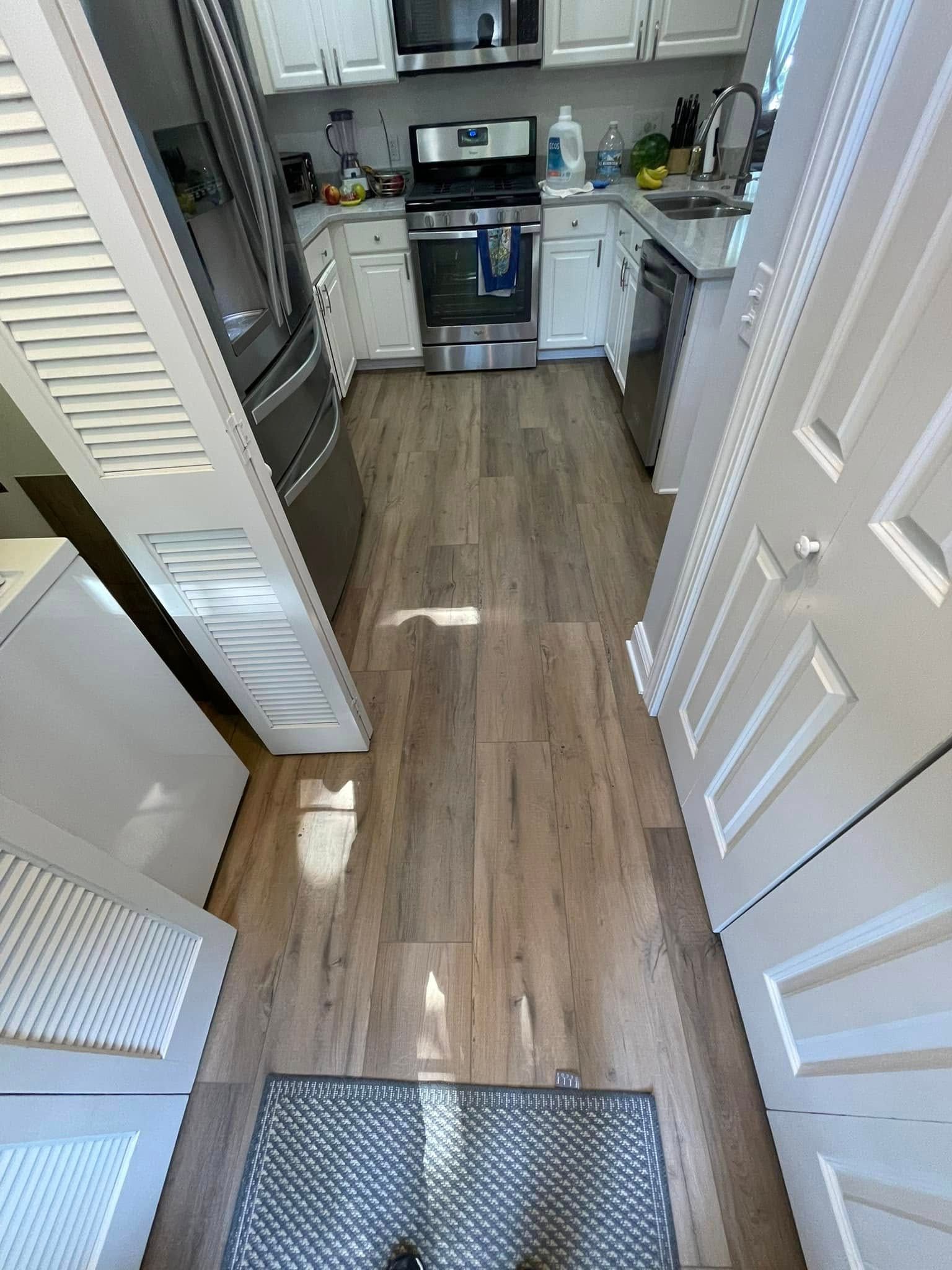 Narrow kitchen with hardwood-look floor, appliances, and white cabinets. A small rug is in the foreground.