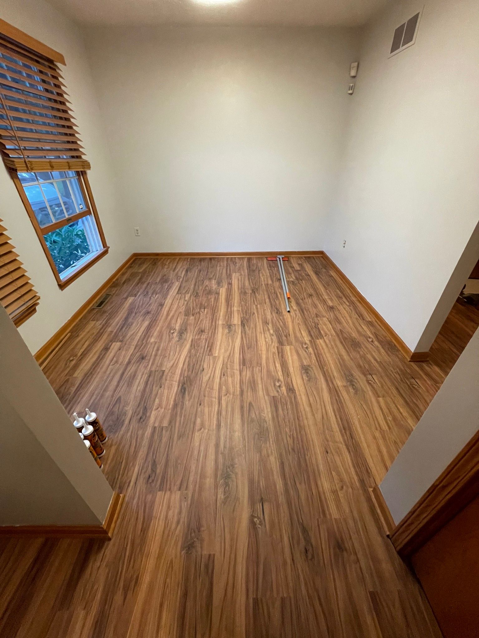Empty room with wood floors and a small window with blinds.