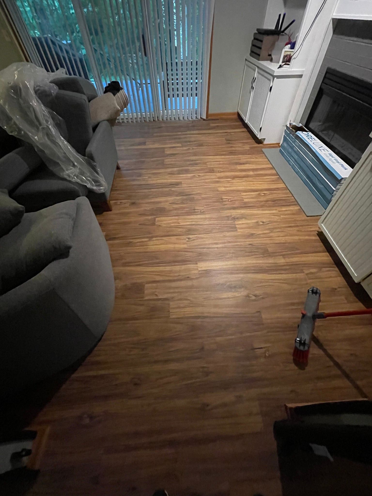 Wood-look flooring in a living room; a gray sofa, fireplace, and sliding glass doors are present.