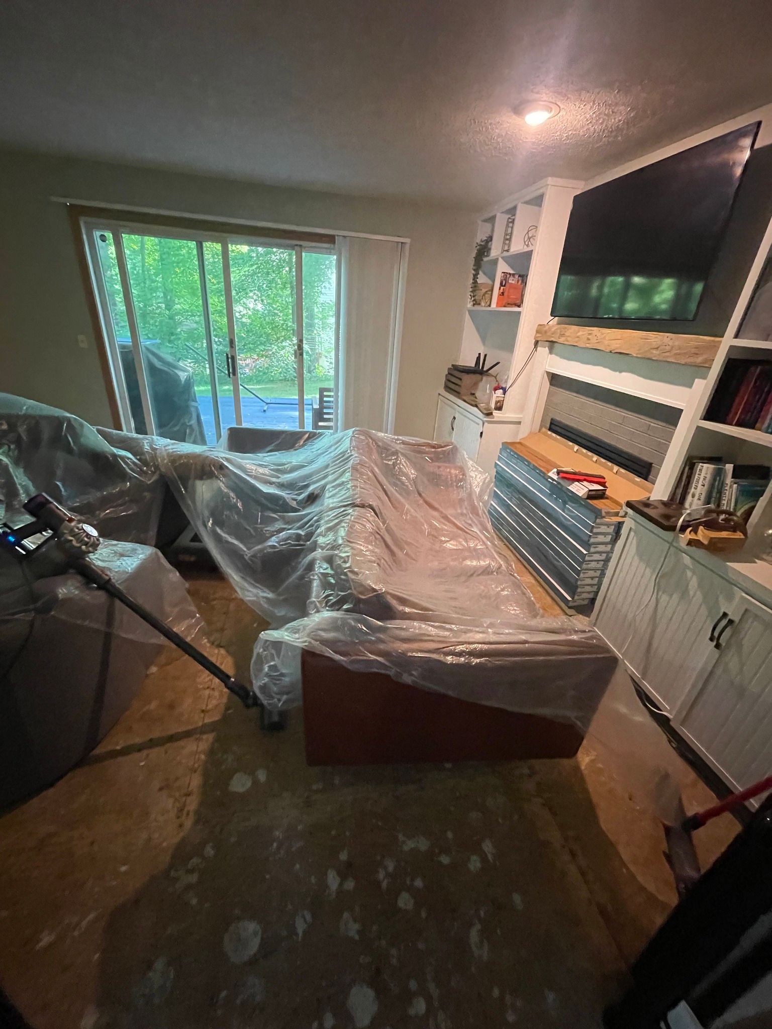Living room with furniture covered in plastic, sliding glass door, TV, and shelves.