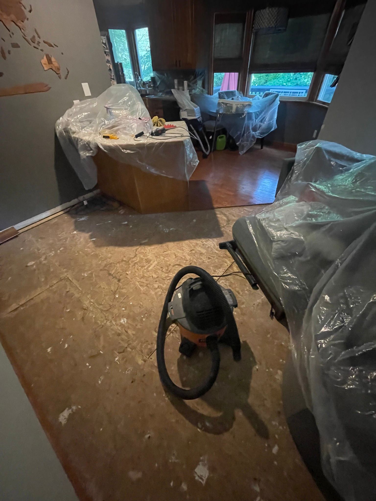 Room undergoing renovation; vacuum cleaner on the floor, furniture and countertops covered in plastic sheeting.
