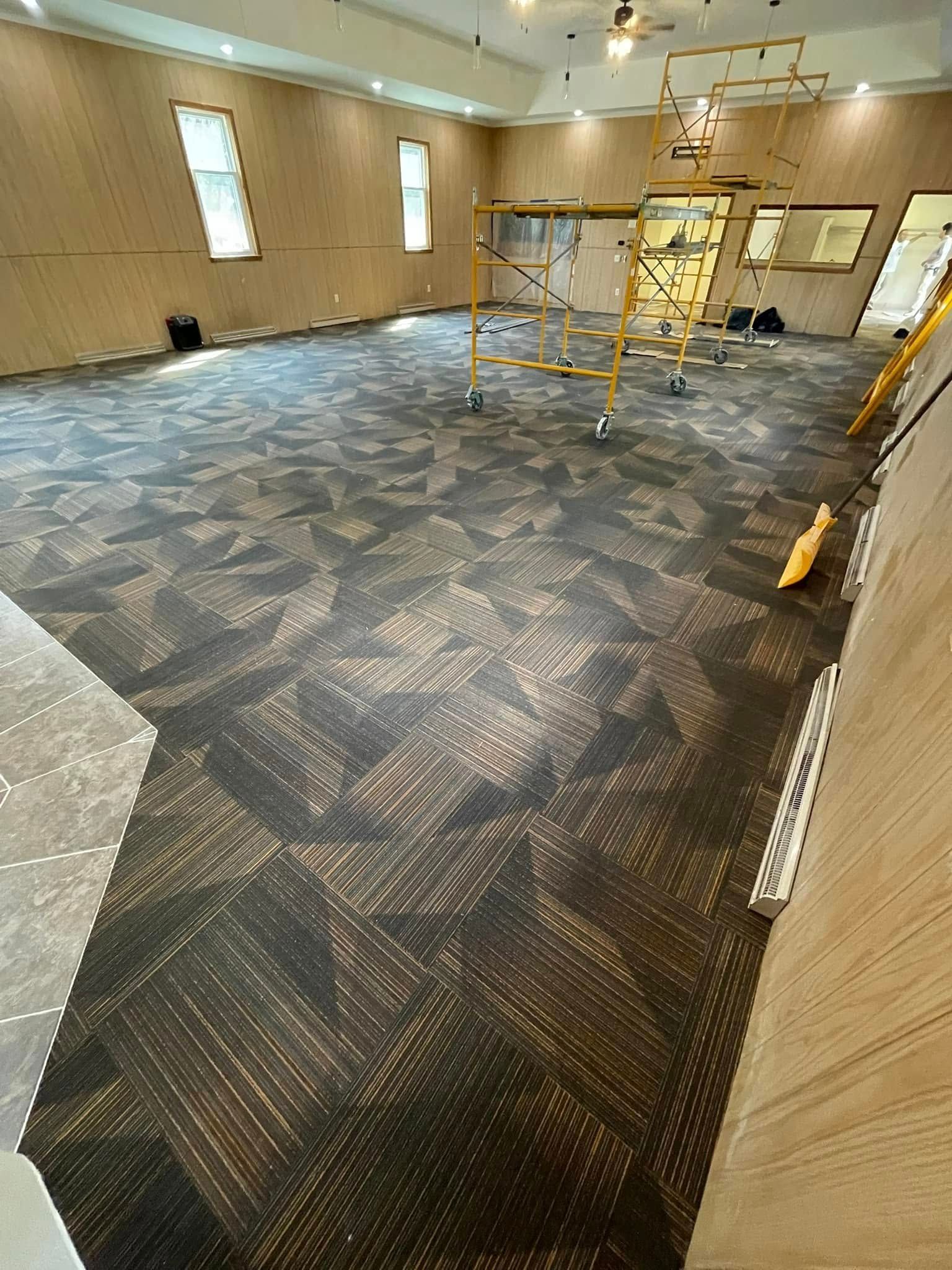 Room with patterned carpet, wooden walls, scaffolding, and two windows.