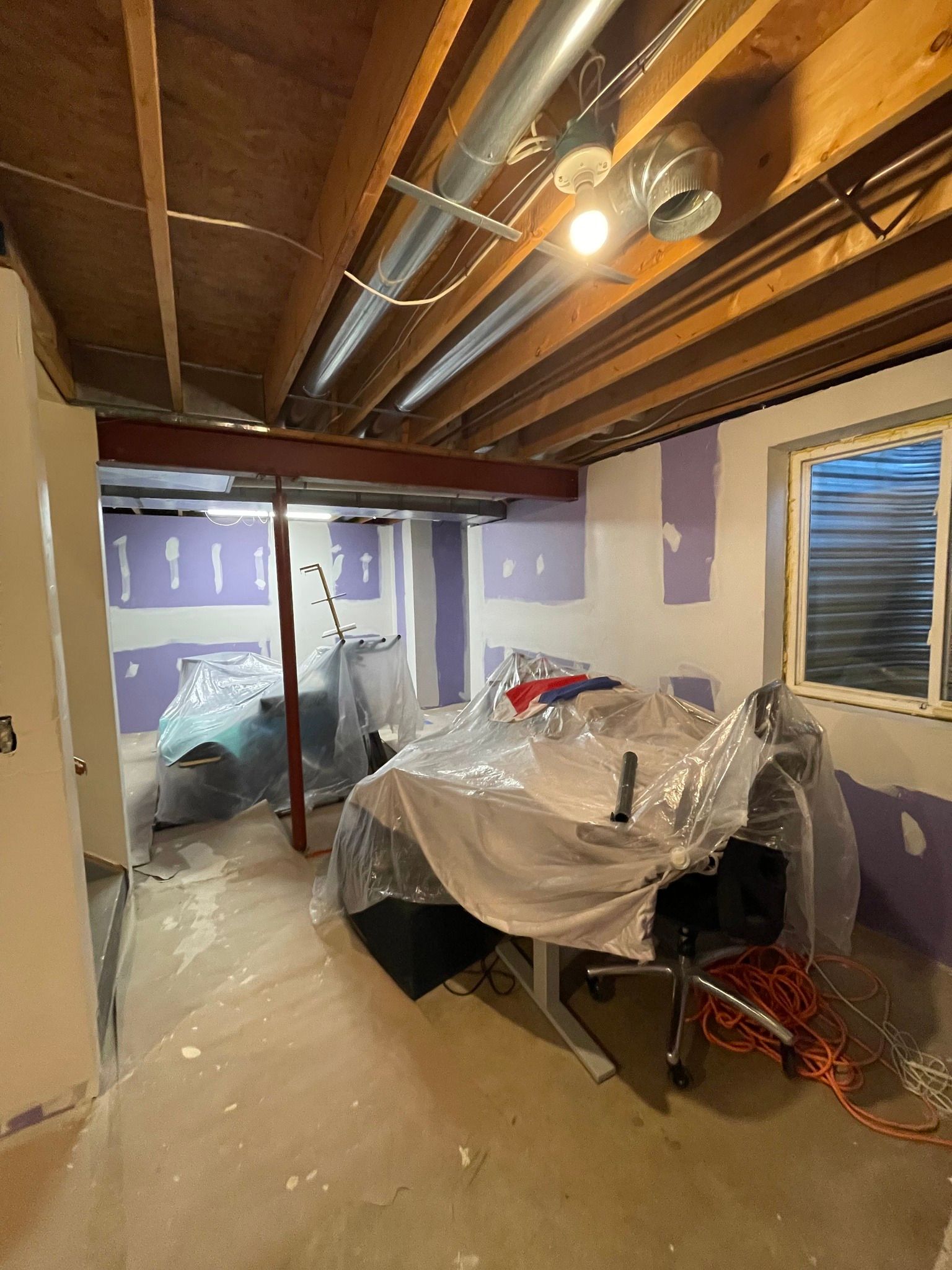 Basement under construction; drywall partially installed. Exposed ceiling beams, ductwork, and covered furniture.