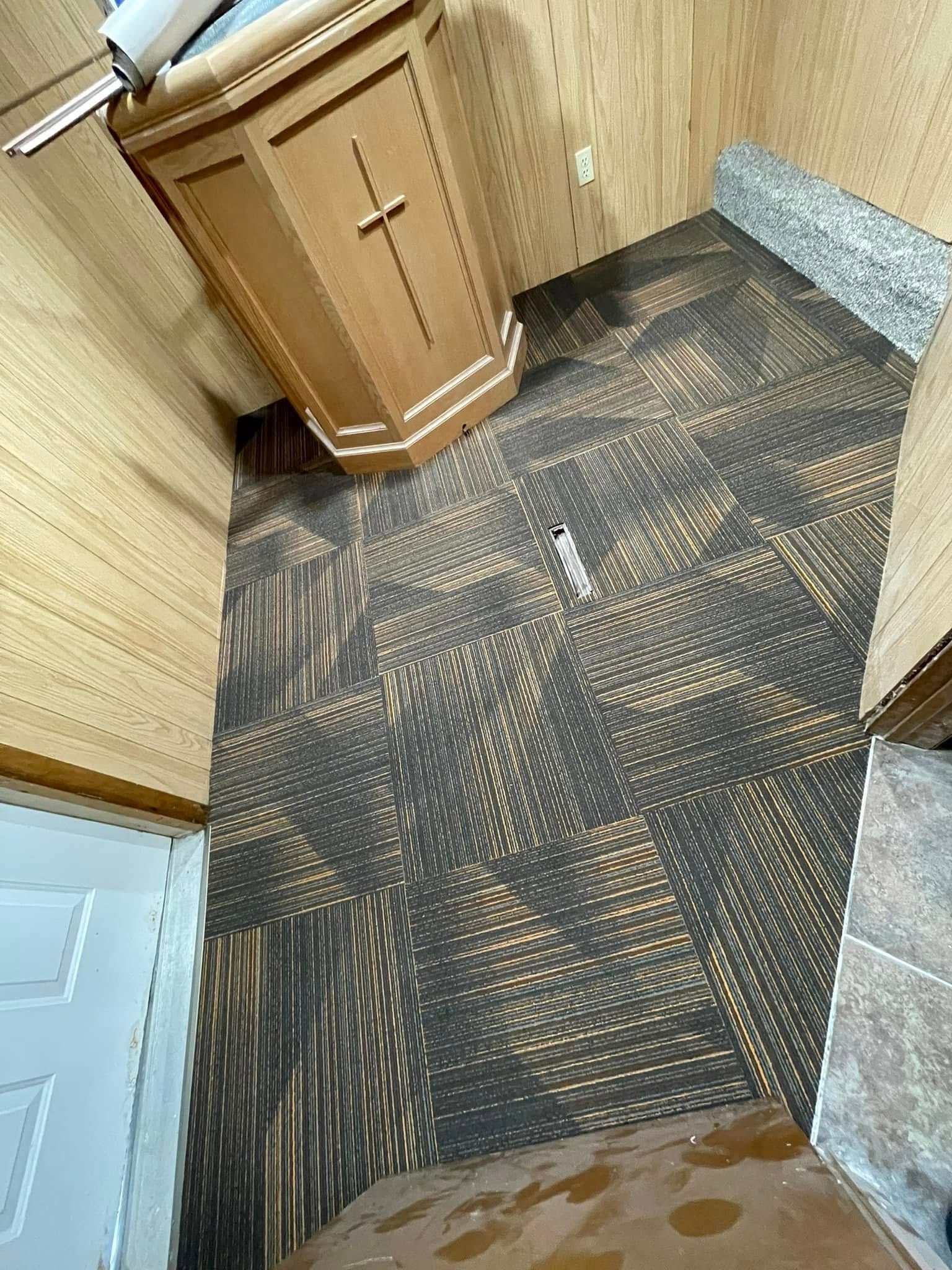 Wooden podium with cross, in room with patterned carpet and side door.