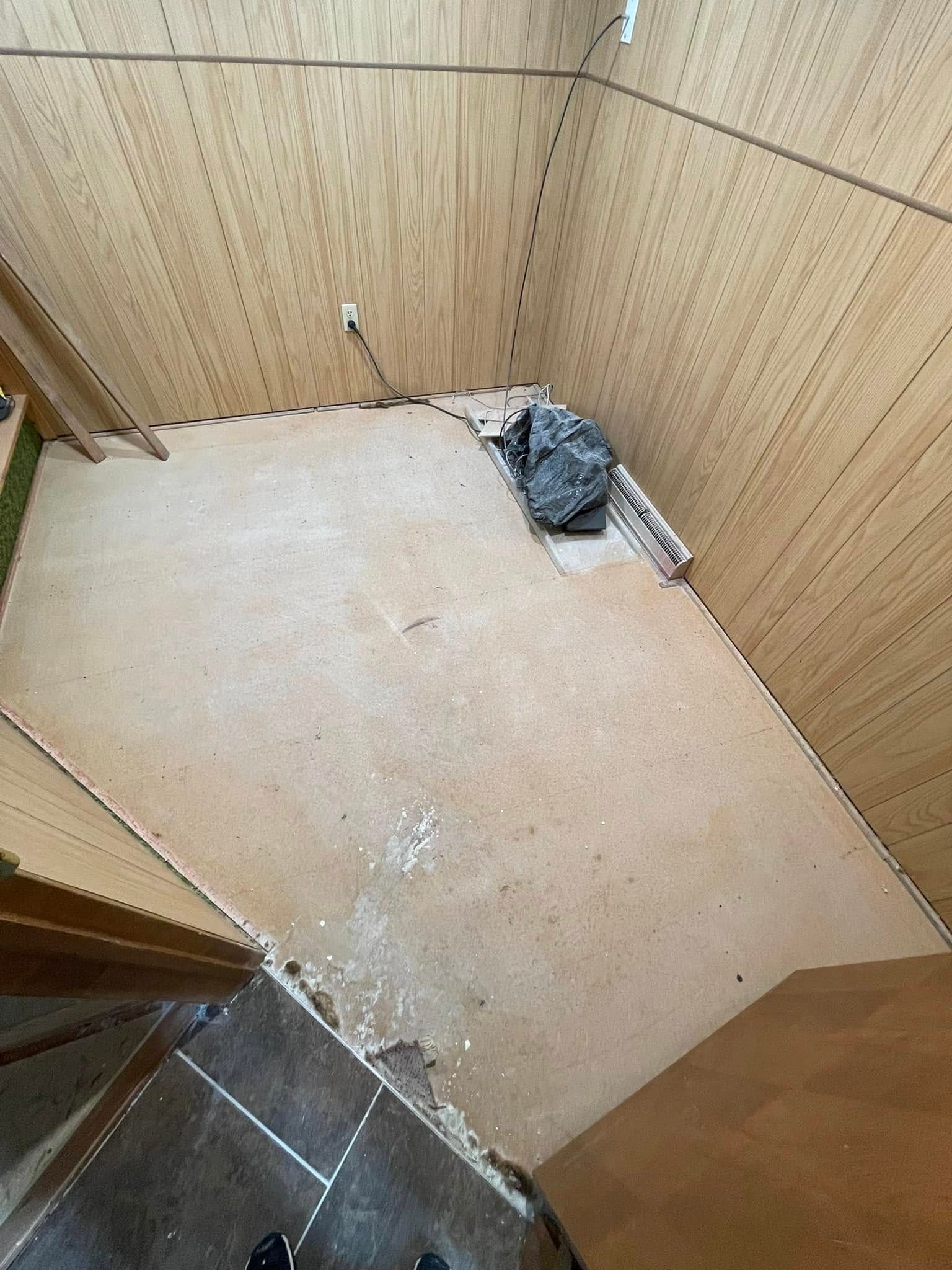 Room corner with brown paneling, light beige floor, and debris.
