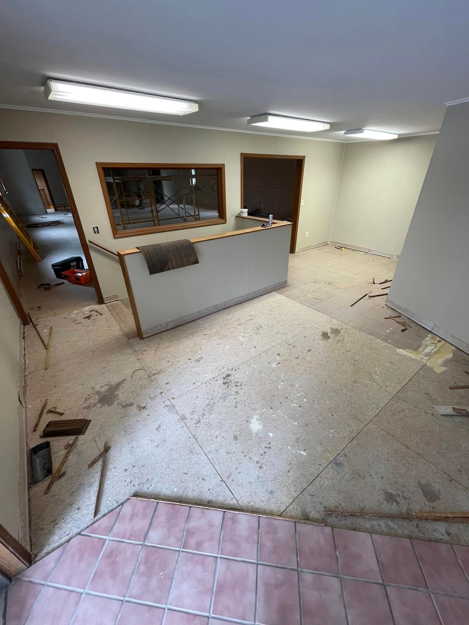 Interior of a room under renovation. Demolished floor, white walls, counter, doors, and a small opening.