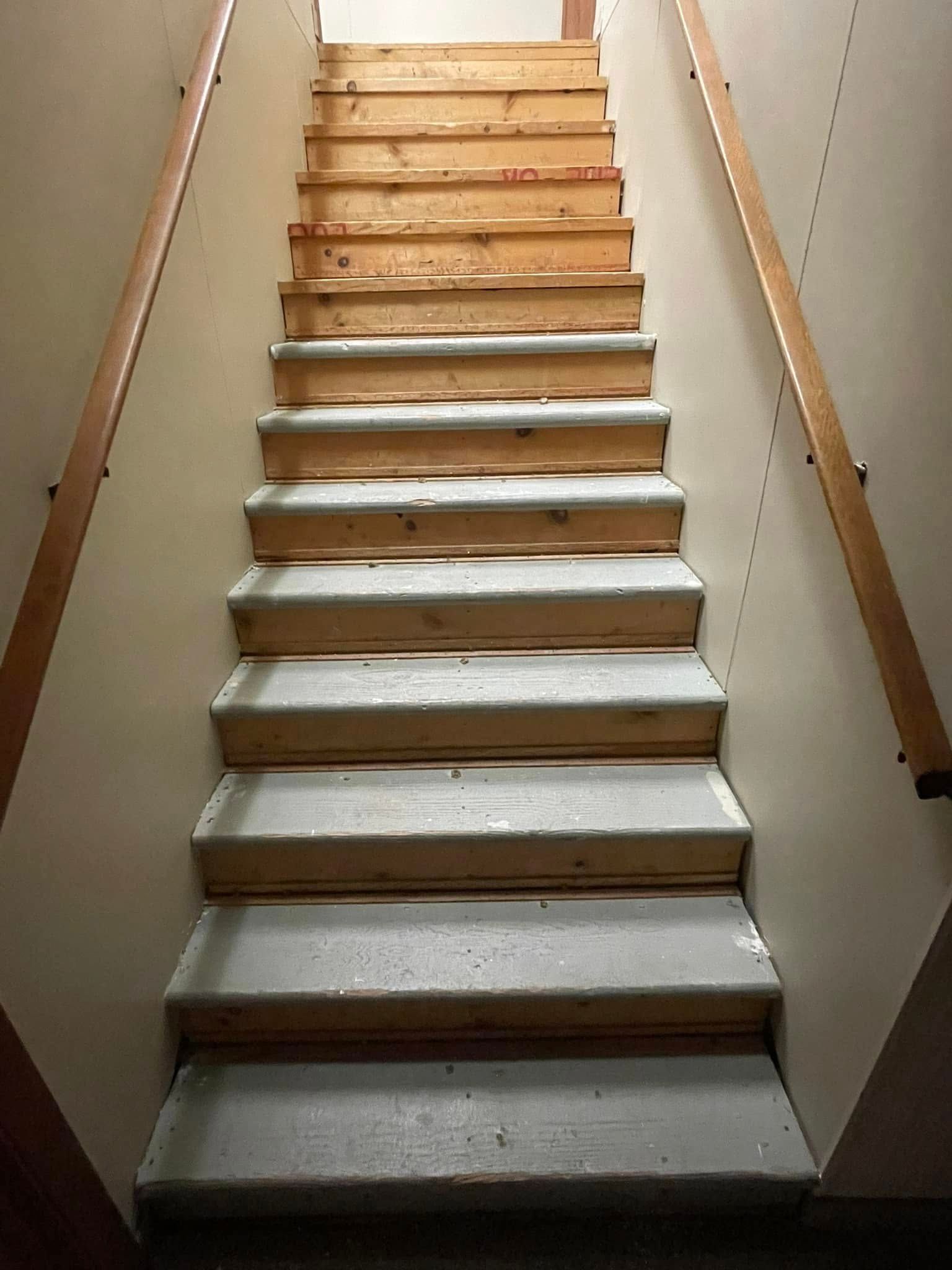 Staircase with wooden handrails and steps. Some steps are wood, some are covered with concrete.