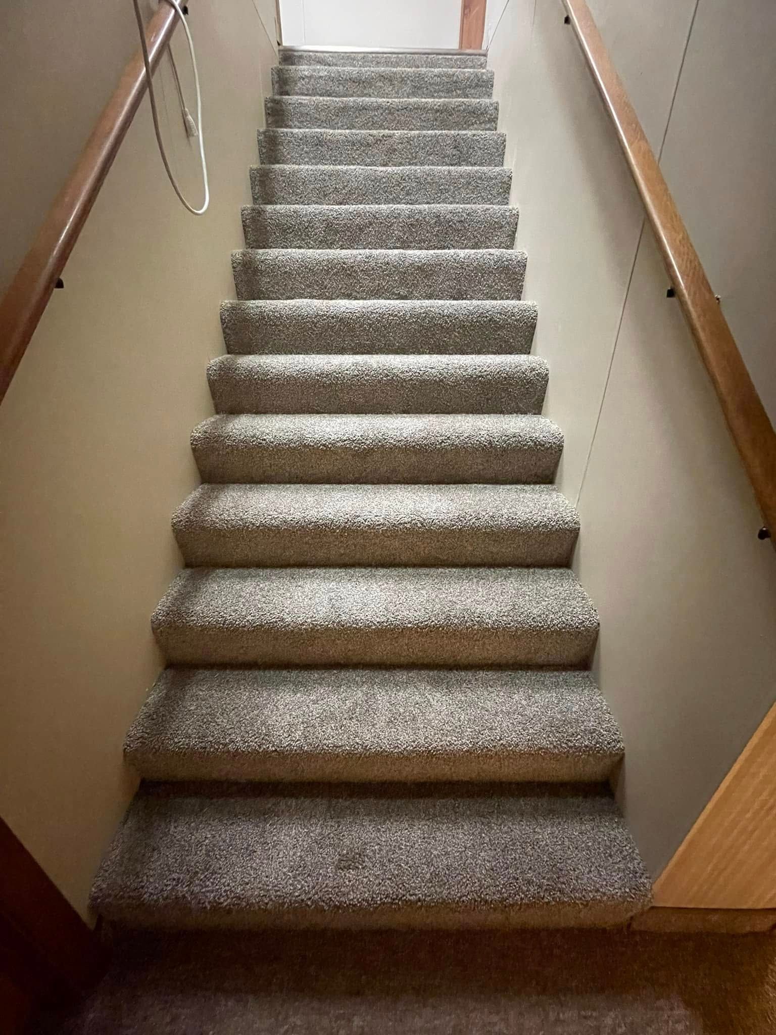 Staircase with carpeted steps leading upwards. Wooden handrails line both sides. Beige walls surround.