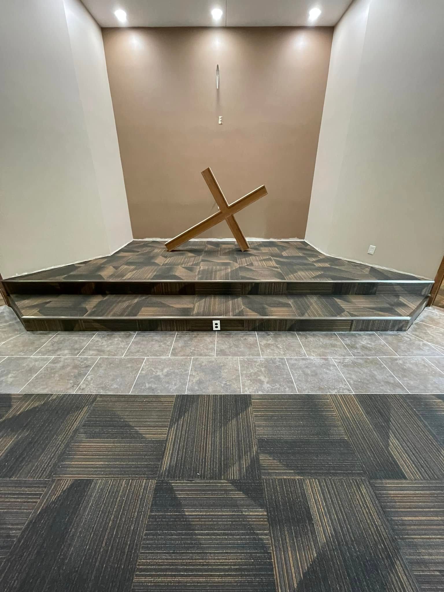 Wooden cross on a multi-tiered platform; neutral-toned walls, and patterned floor.