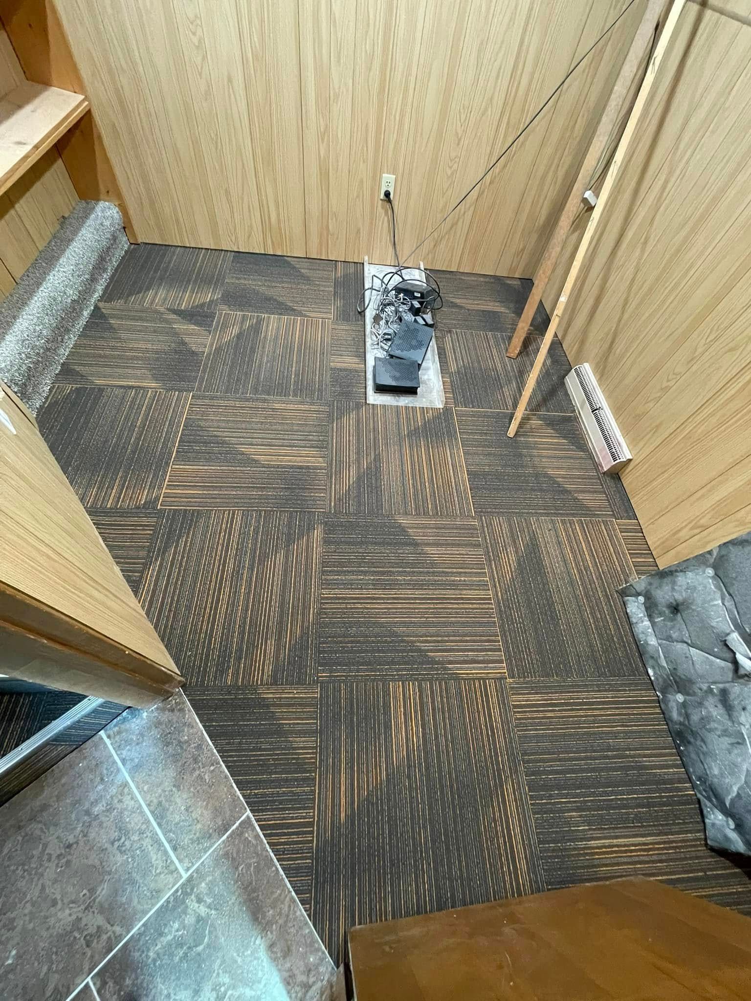 Interior of a small room with wood paneling and patterned floor tiles; heater in center.