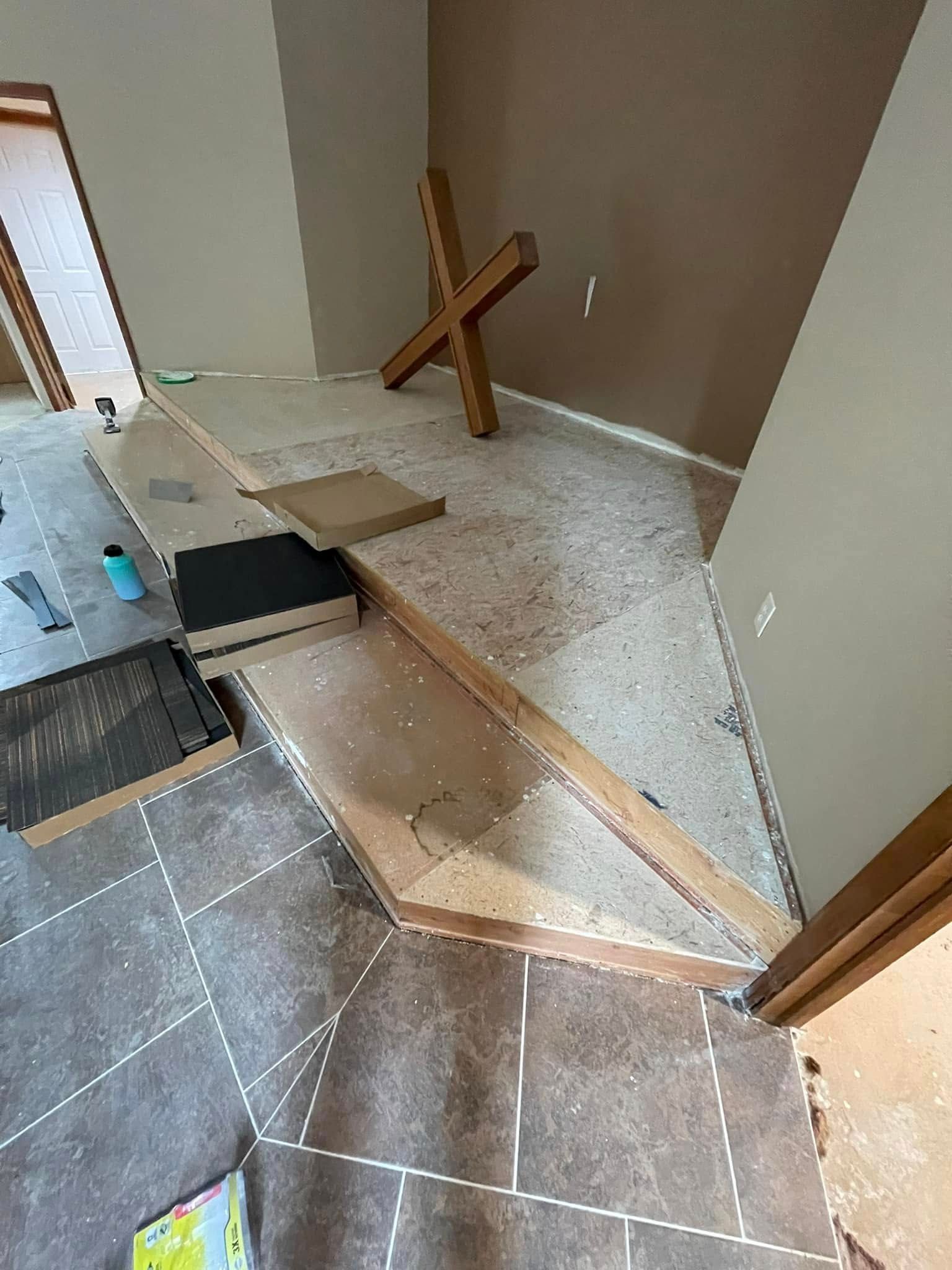 Room under renovation. Wooden cross, flooring materials, and exposed subfloor.