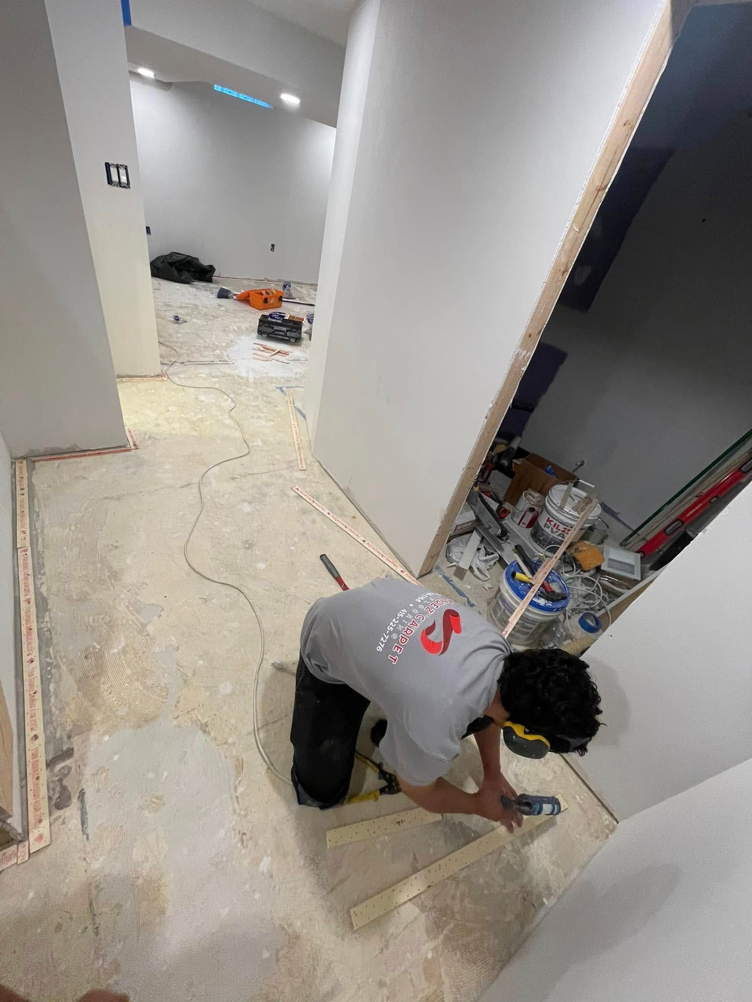 Person installing wood trim in a hallway under construction; tools and materials are visible.