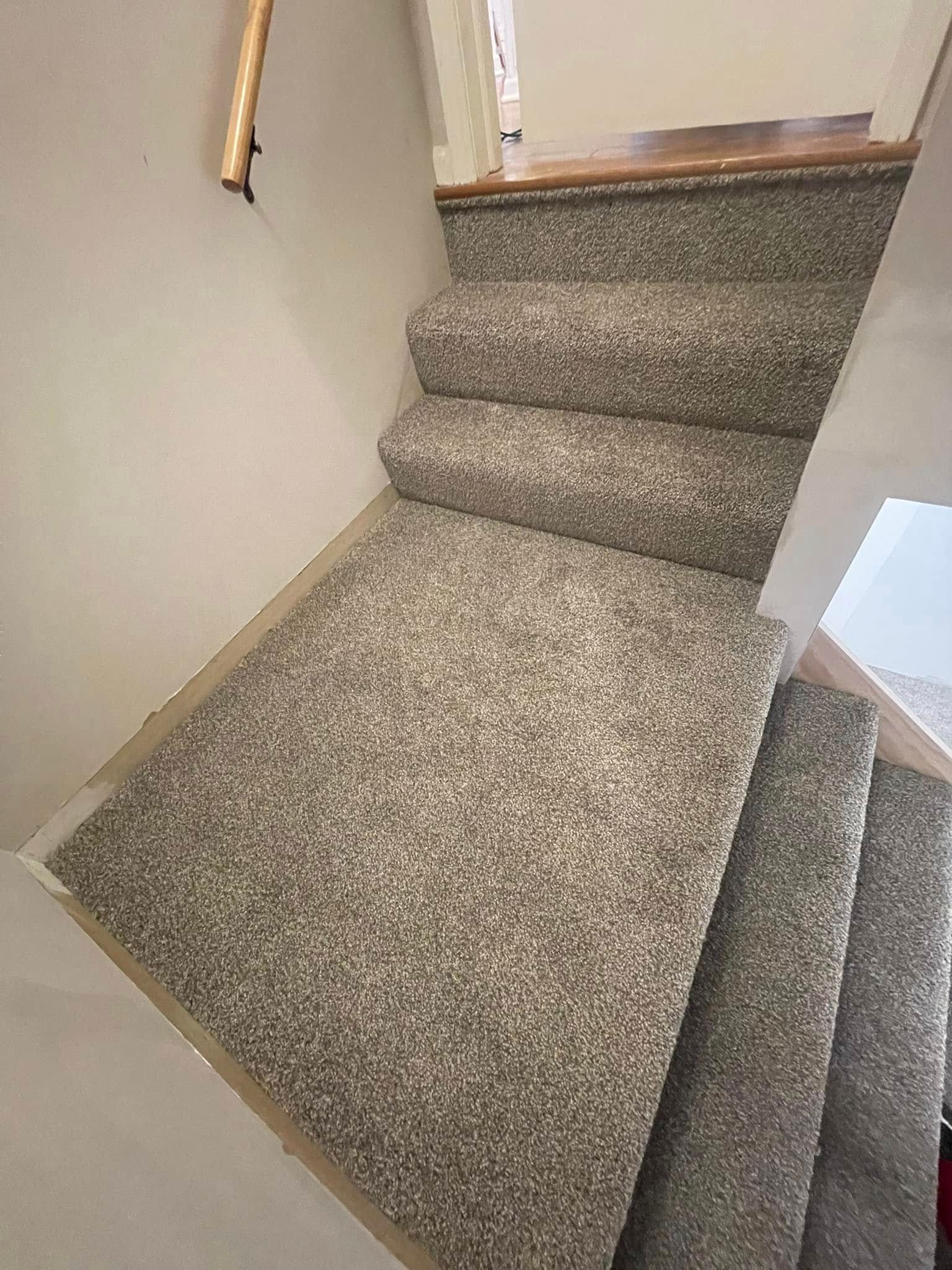 Staircase with gray carpet, leading upwards. Wooden handrail on the left.