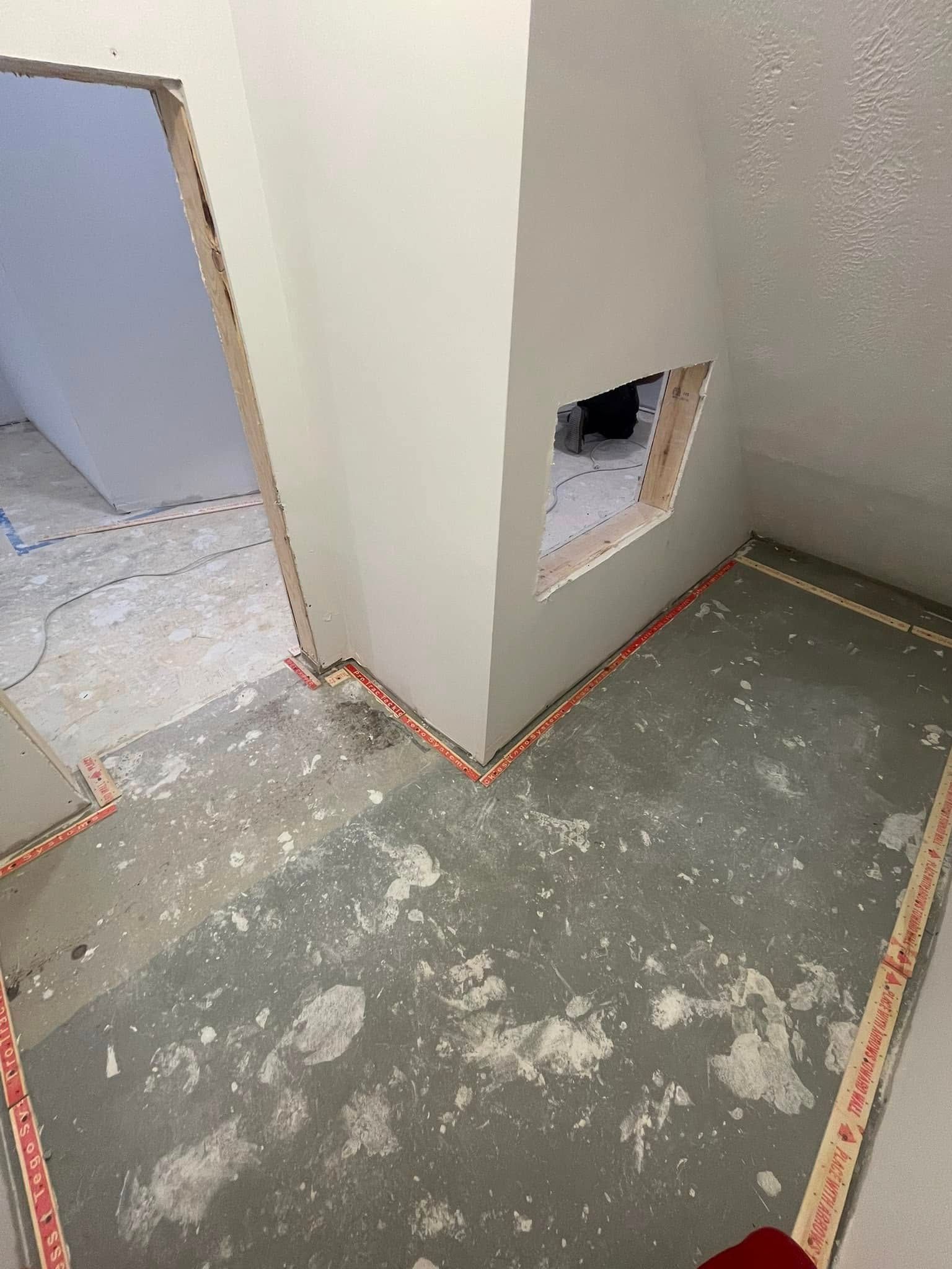 Interior renovation: unfinished room with exposed walls, doorway, and flooring. Pink tape lines edges.