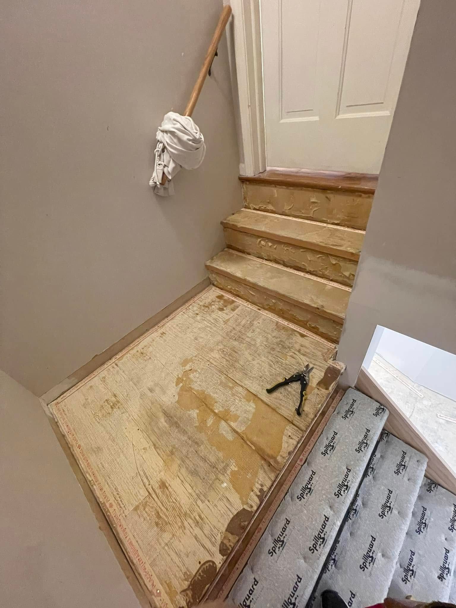 Staircase being renovated; old carpet removed, wood exposed. Handrail with mop attached.