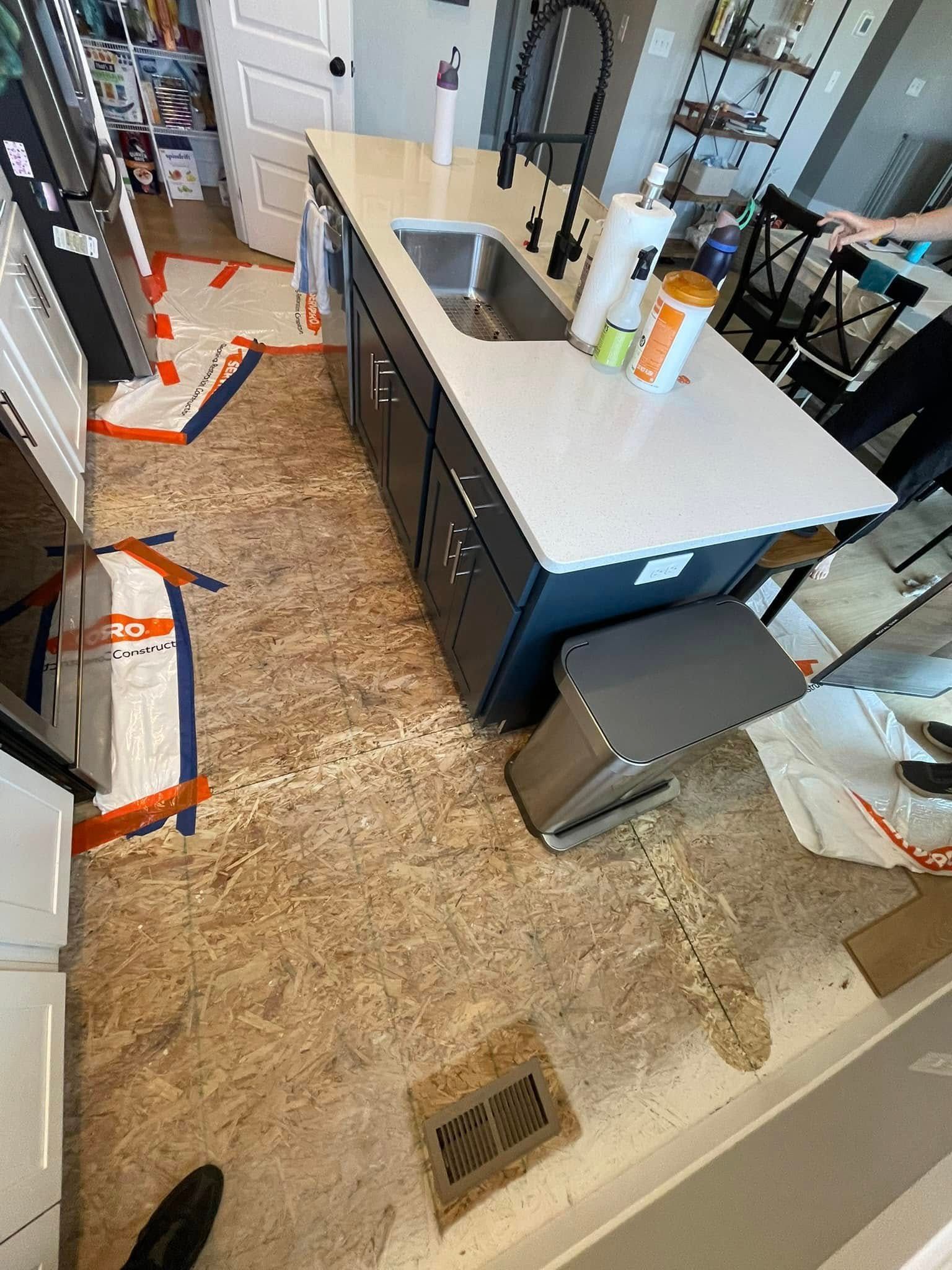 Kitchen with island and damaged flooring; construction in progress.