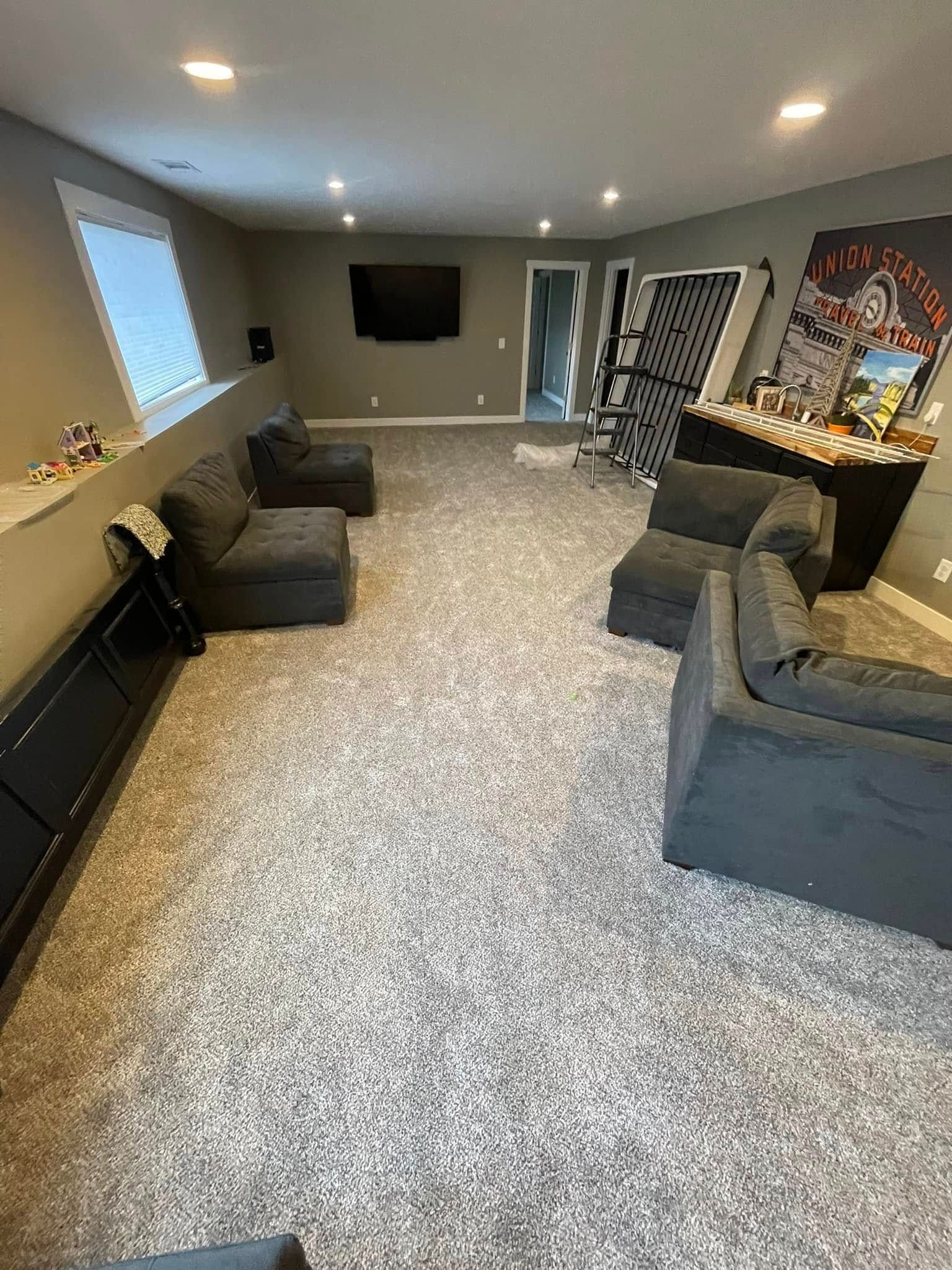 Gray carpeted basement with gray modular sofas, TV, and decorative items.