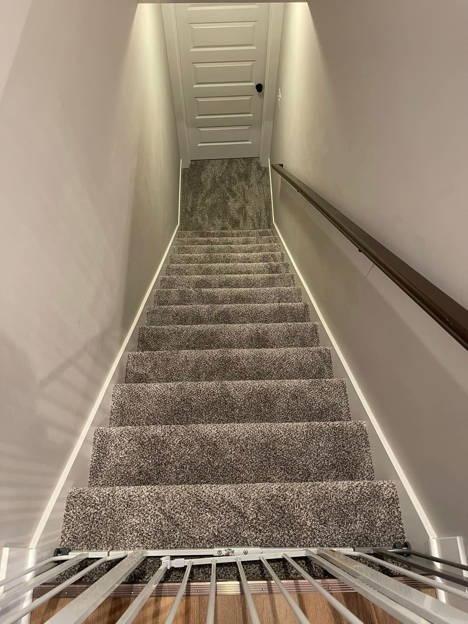Staircase with carpet and handrail, viewed from above, with bright lighting along the sides.