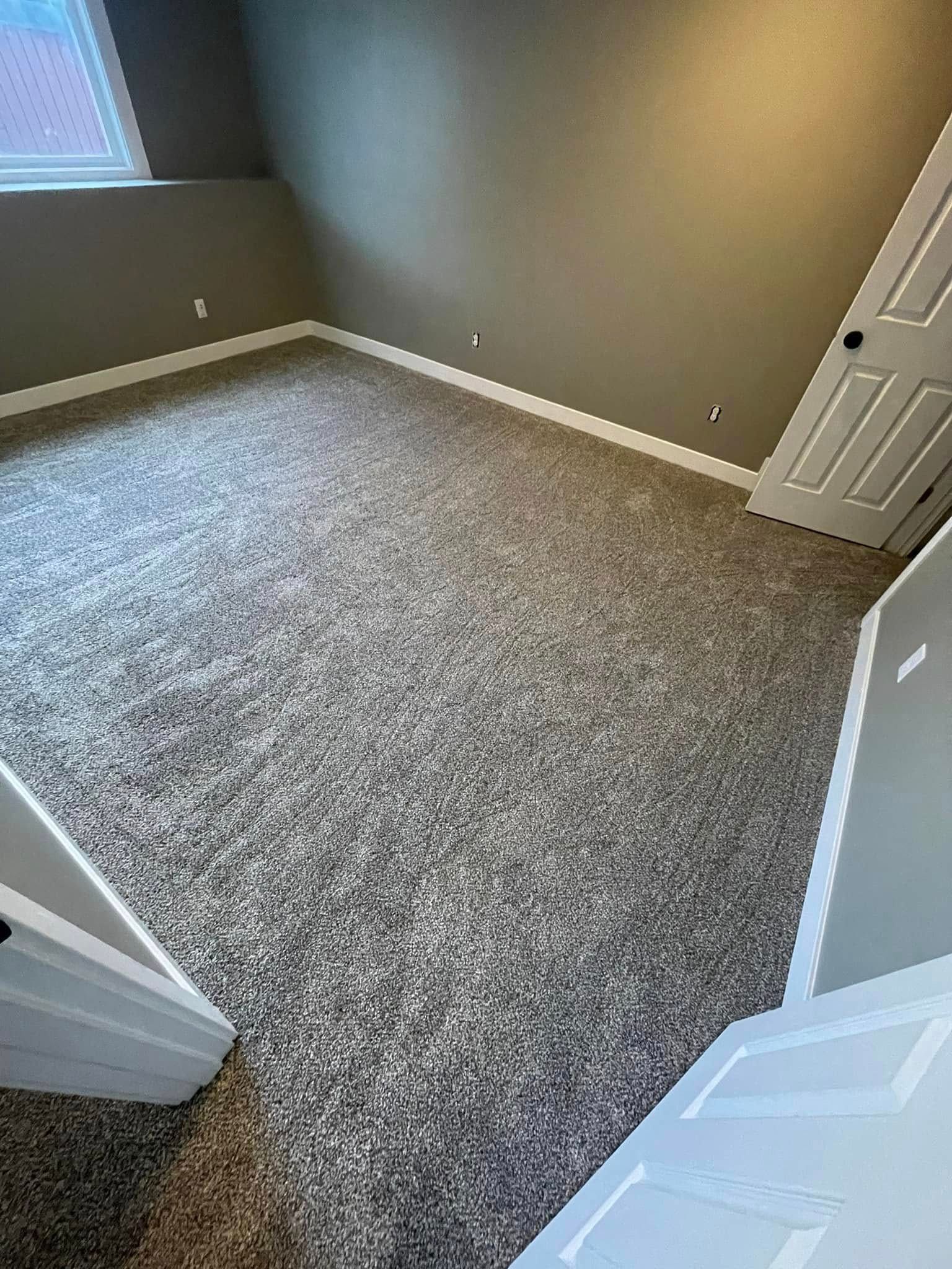 Empty room with gray carpet, walls, and white trim. A closed white door is on the right.