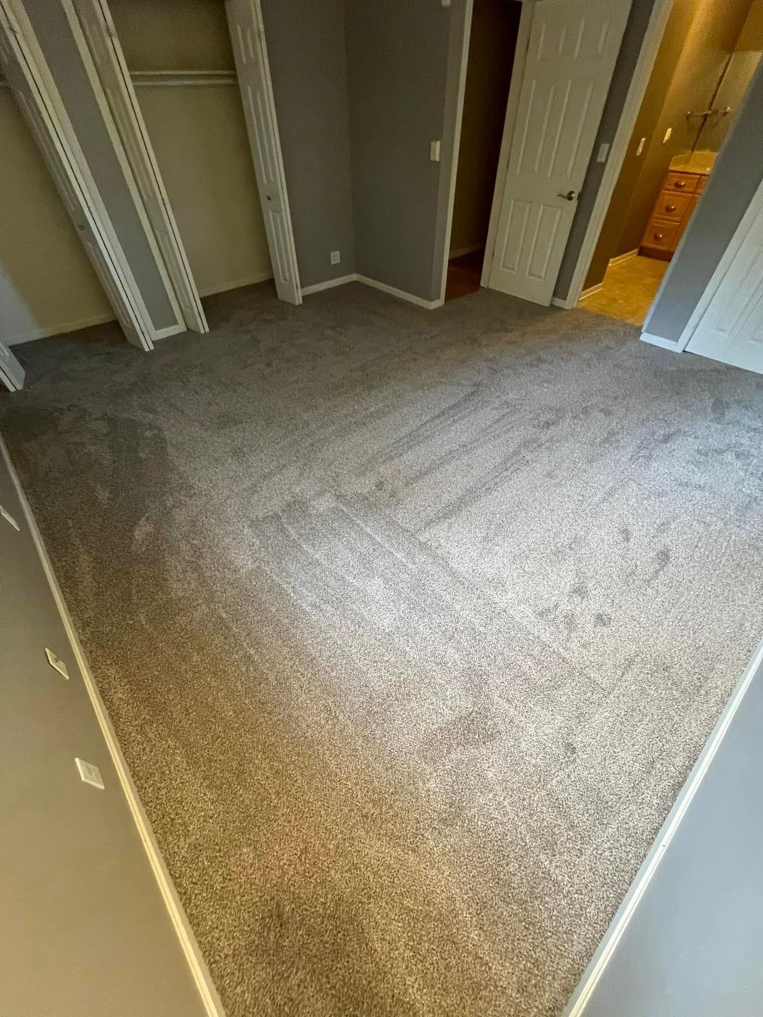 A room with gray walls and a speckled carpet. White trim outlines the room's edges. A doorway is visible.