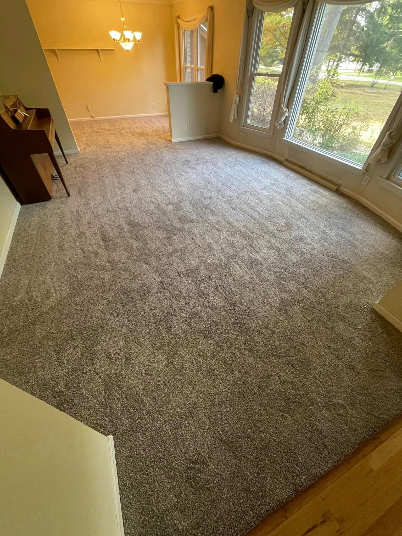 Room with new gray carpet, bright windows, and a doorway leading to another room.