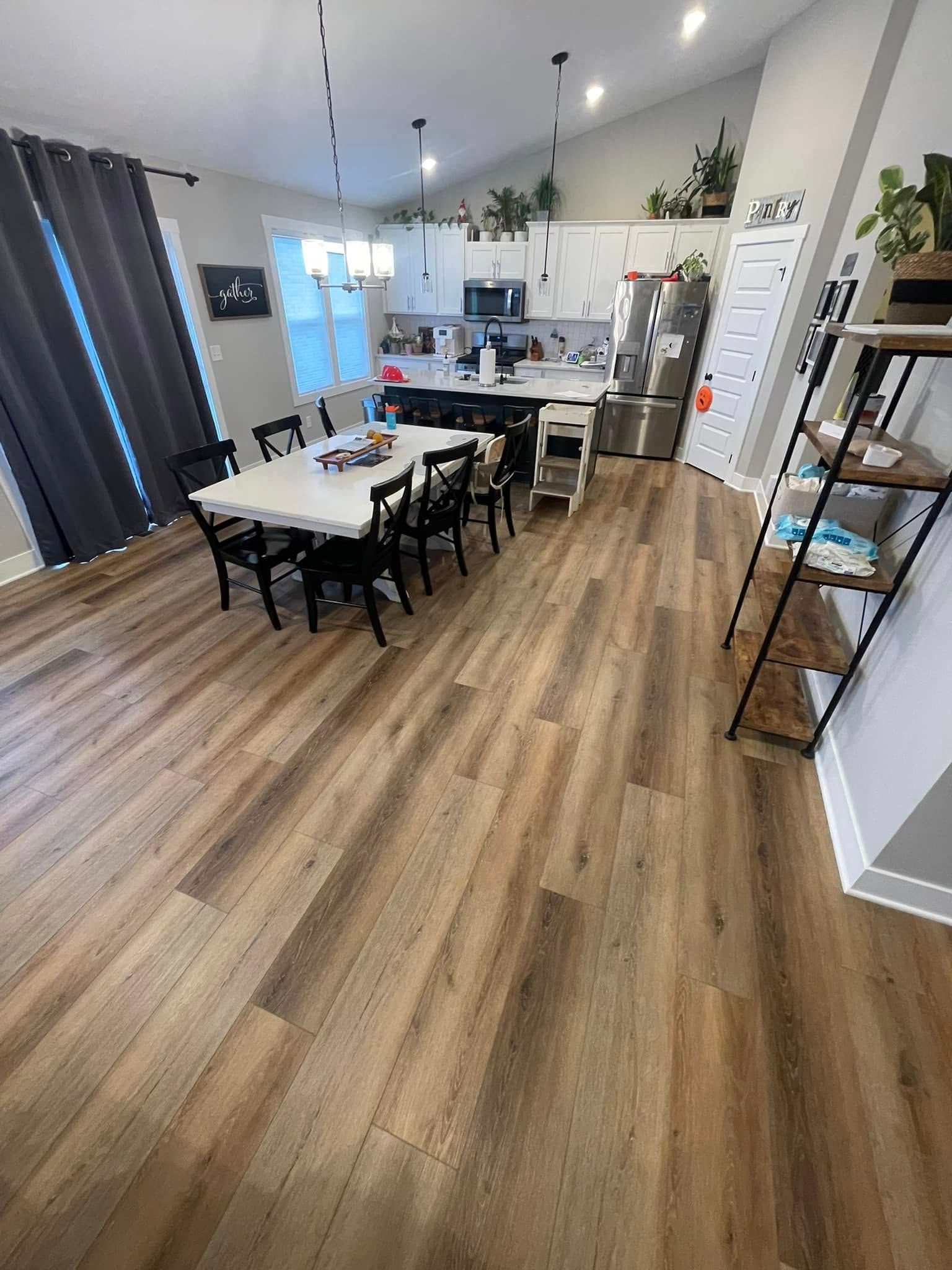 Open-plan kitchen/dining room with wood floors. Table with chairs, kitchen island, and shelves with plants.
