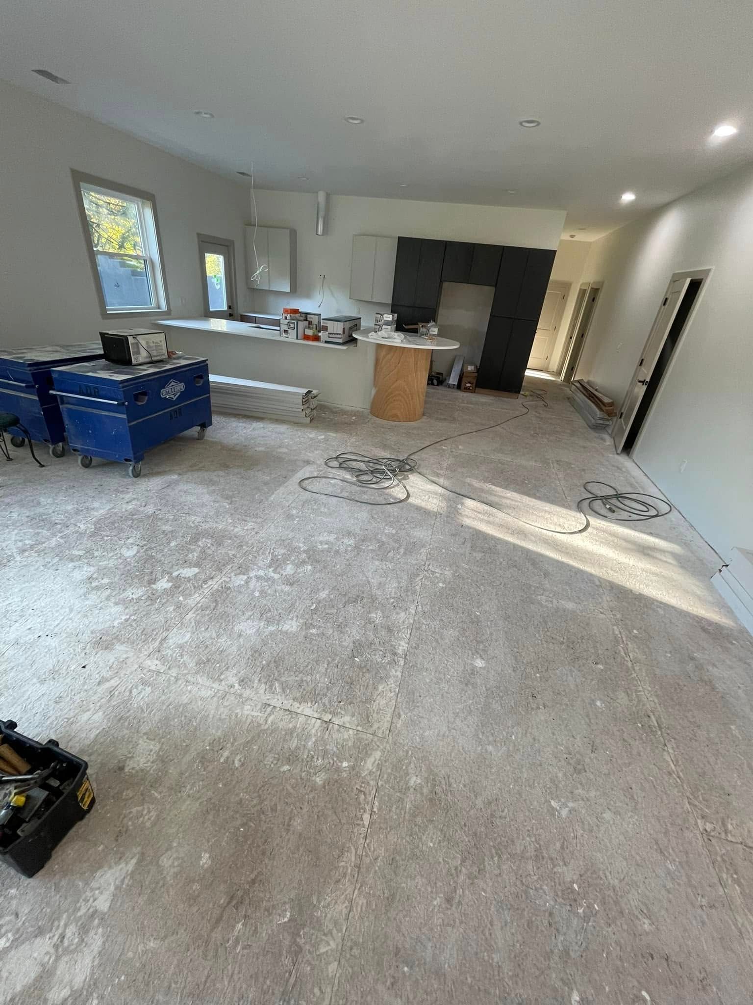 Interior of a room under construction, with exposed concrete floor, tools, and a partial kitchen setup.
