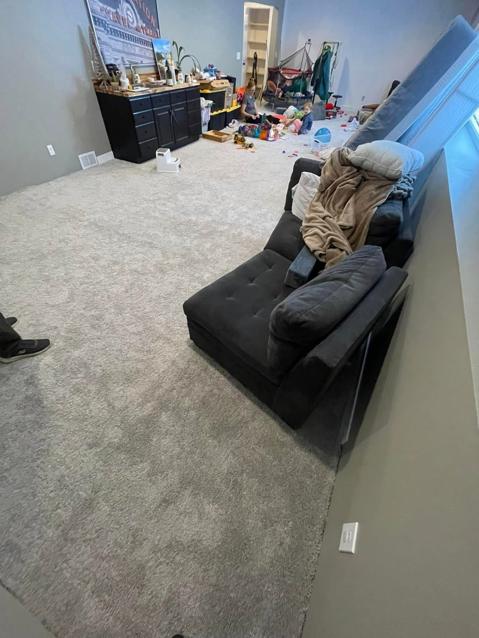 Gray carpeted room with black couch, toys, and cluttered shelves.