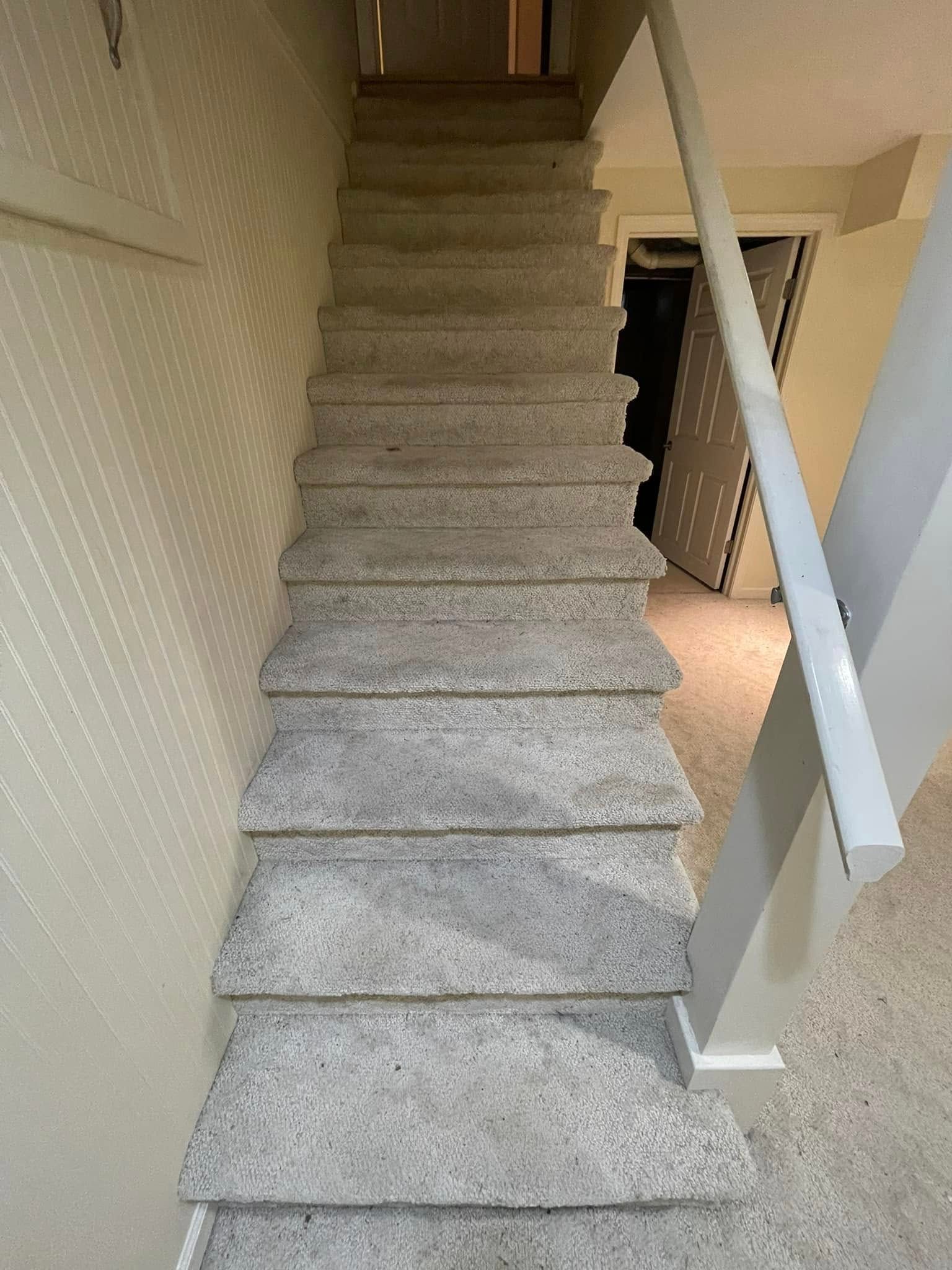 Staircase with gray carpet leading upwards; white walls and a handrail are visible.