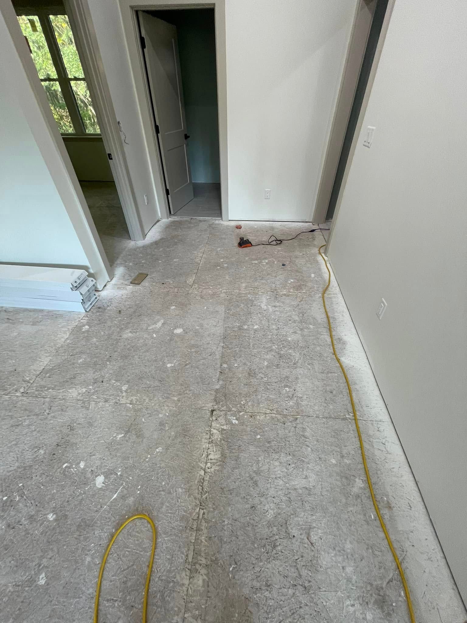 Concrete floor with debris and exposed wiring in a room with doorways and white walls.