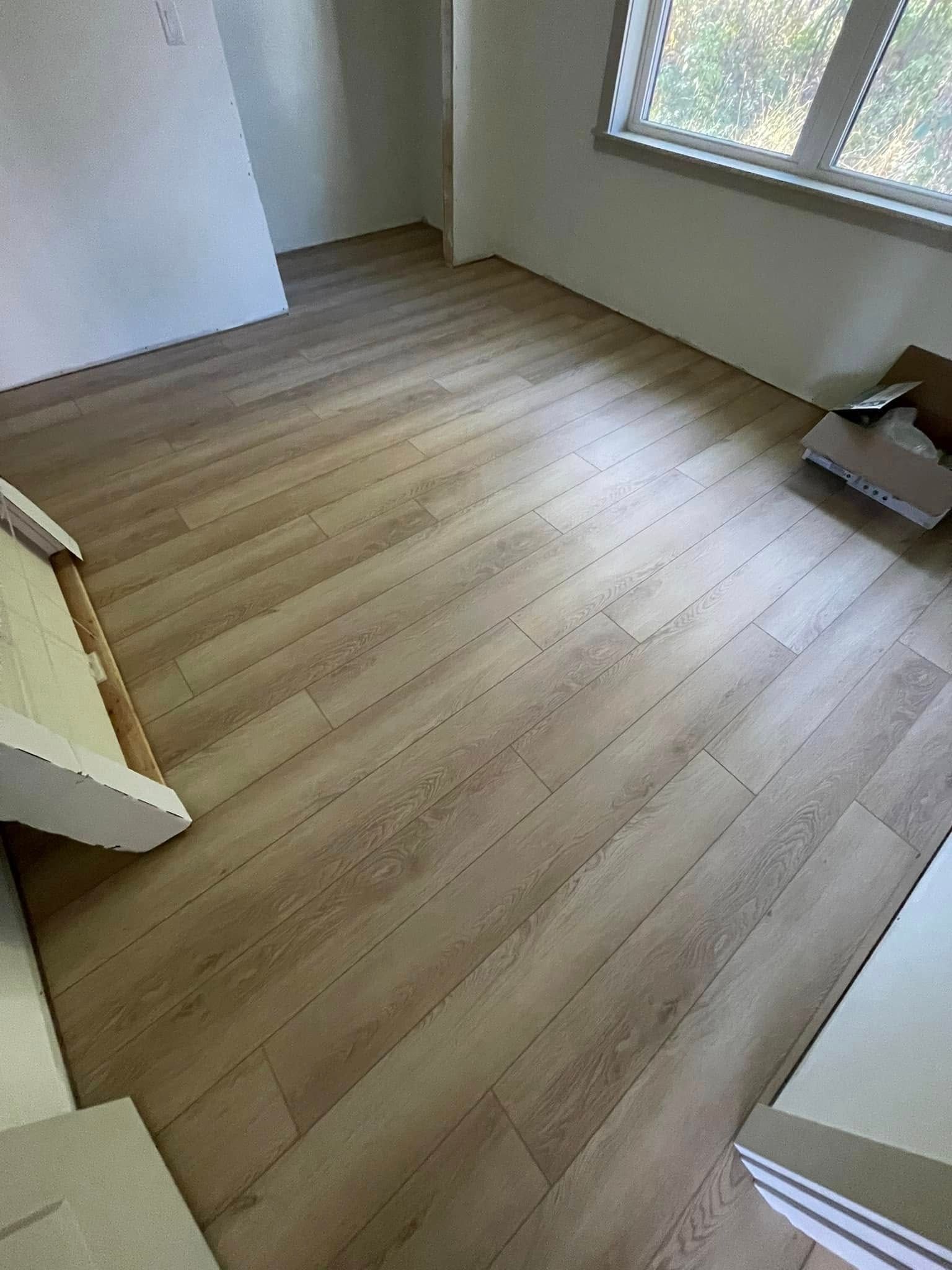 Room with light wood-look flooring. Partially empty, with a window and a wall visible.