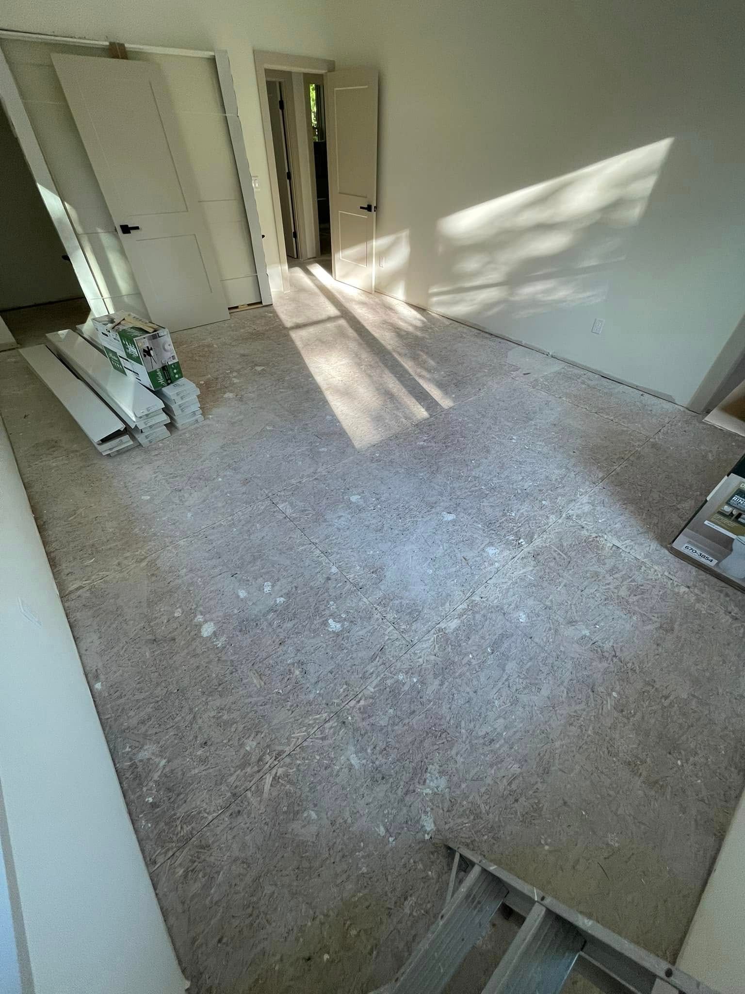 Empty room with concrete floor, two doors, and construction materials on the floor. Sunlight.